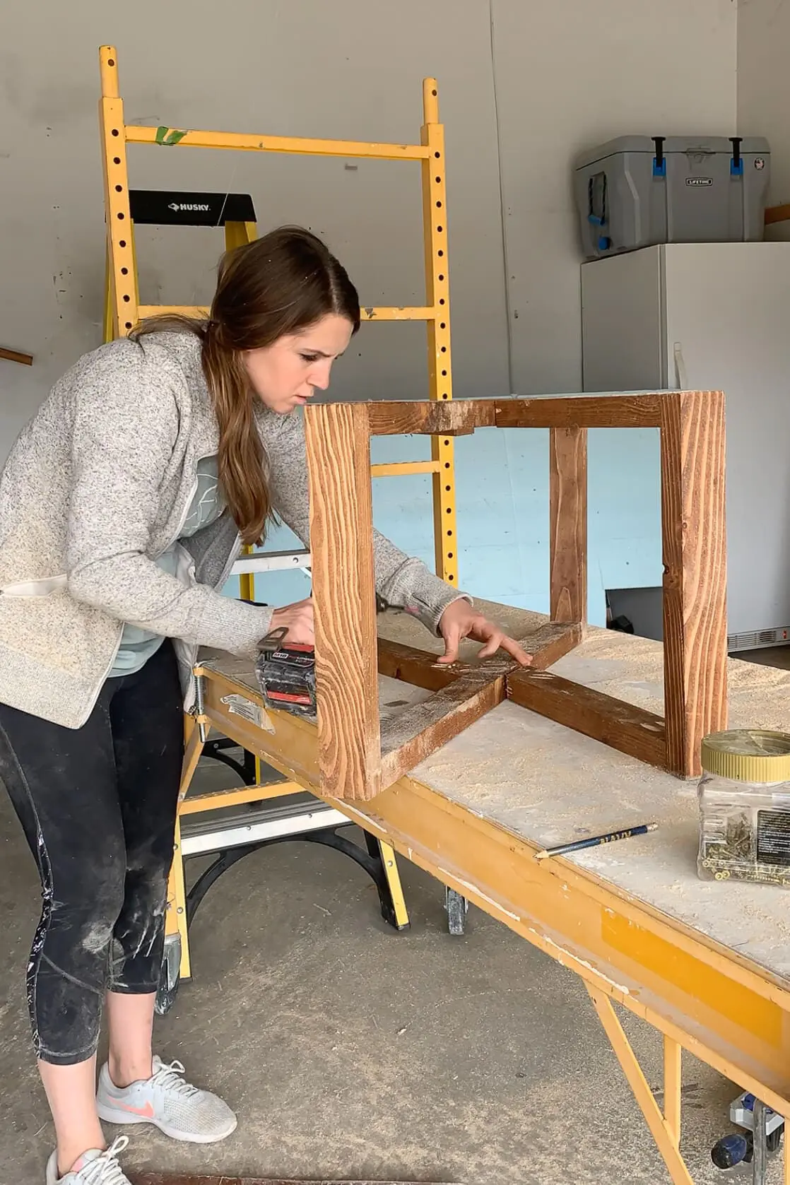 Securing cross supports to the stained wood leg frame during the final base assembly of a DIY coffee table.