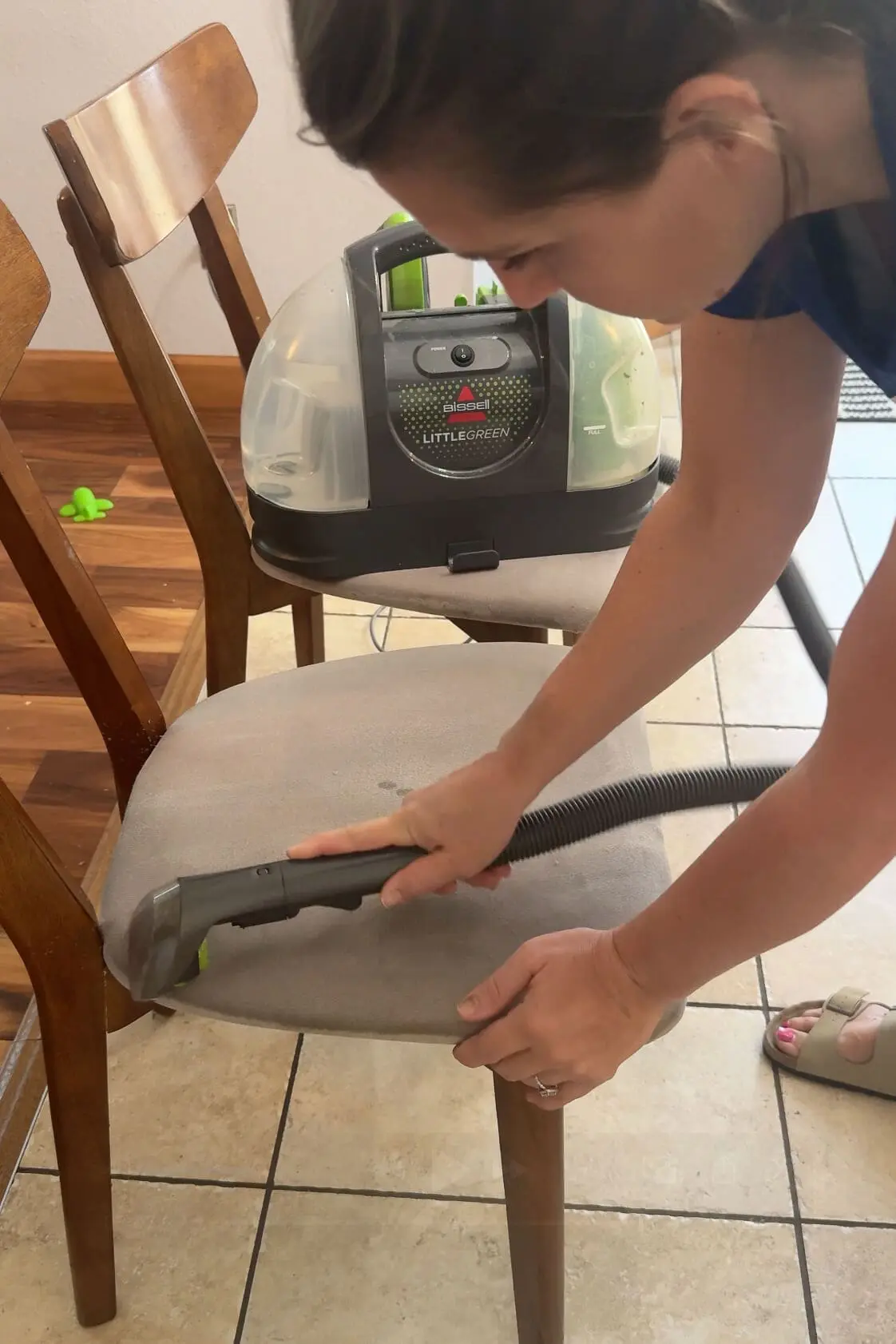 Using a BISSELL Little Green machine to deep clean an upholstered dining chair with a fabric-safe upholstery attachment.