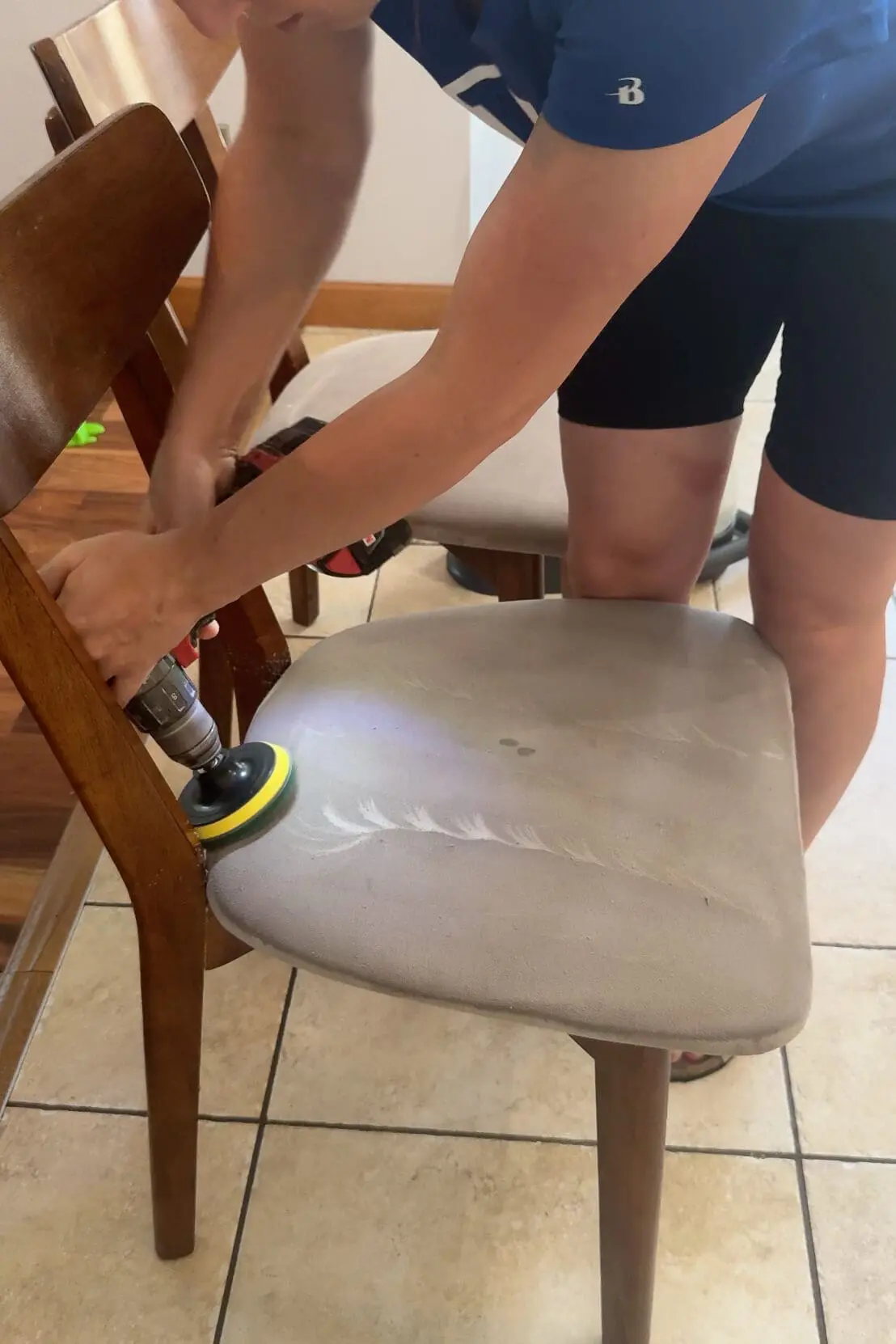 Using a drill brush attachment to deep clean a stained upholstered dining chair seat.