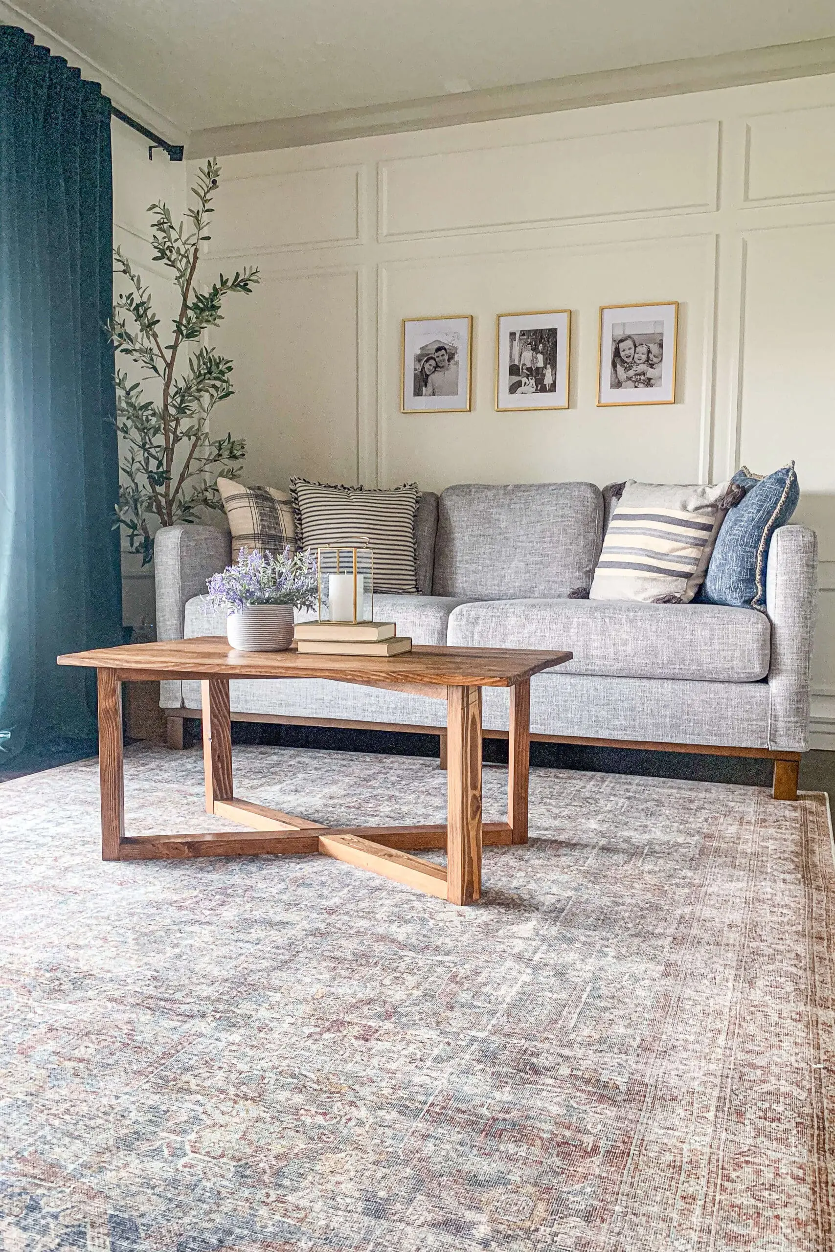 DIY coffee table with a geometric base, styled in a cozy living room featuring a gray sofa, framed black-and-white photos, and vintage-inspired decor.