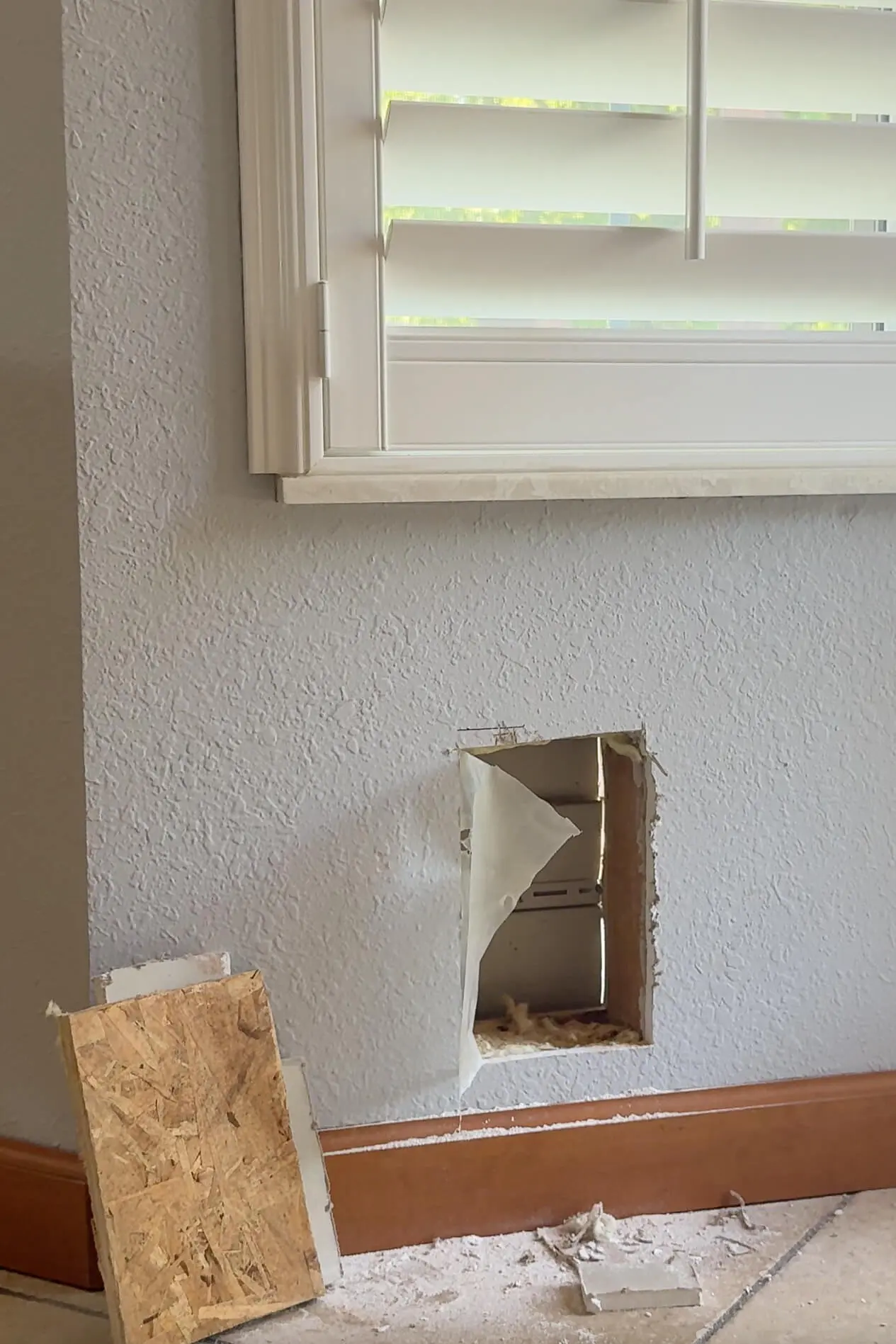 Cutting a hole in the Interior wall with a multitool. The picture shows a fully exposed opening showing drywall, insulation, and wall studs.