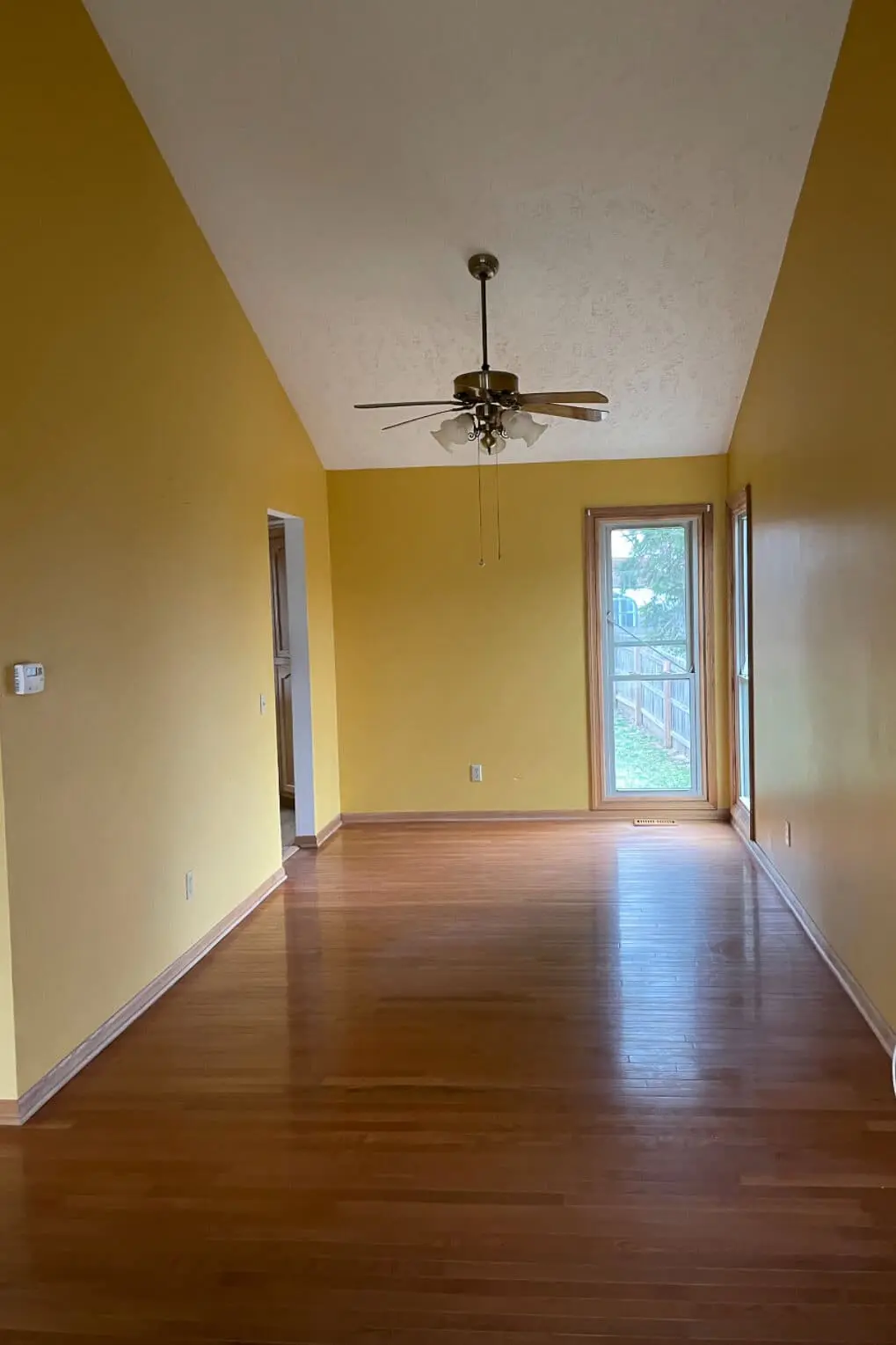Before photo of kitchen and dining space with yellow walls, vaulted ceiling, and wood floors before DIY renovation