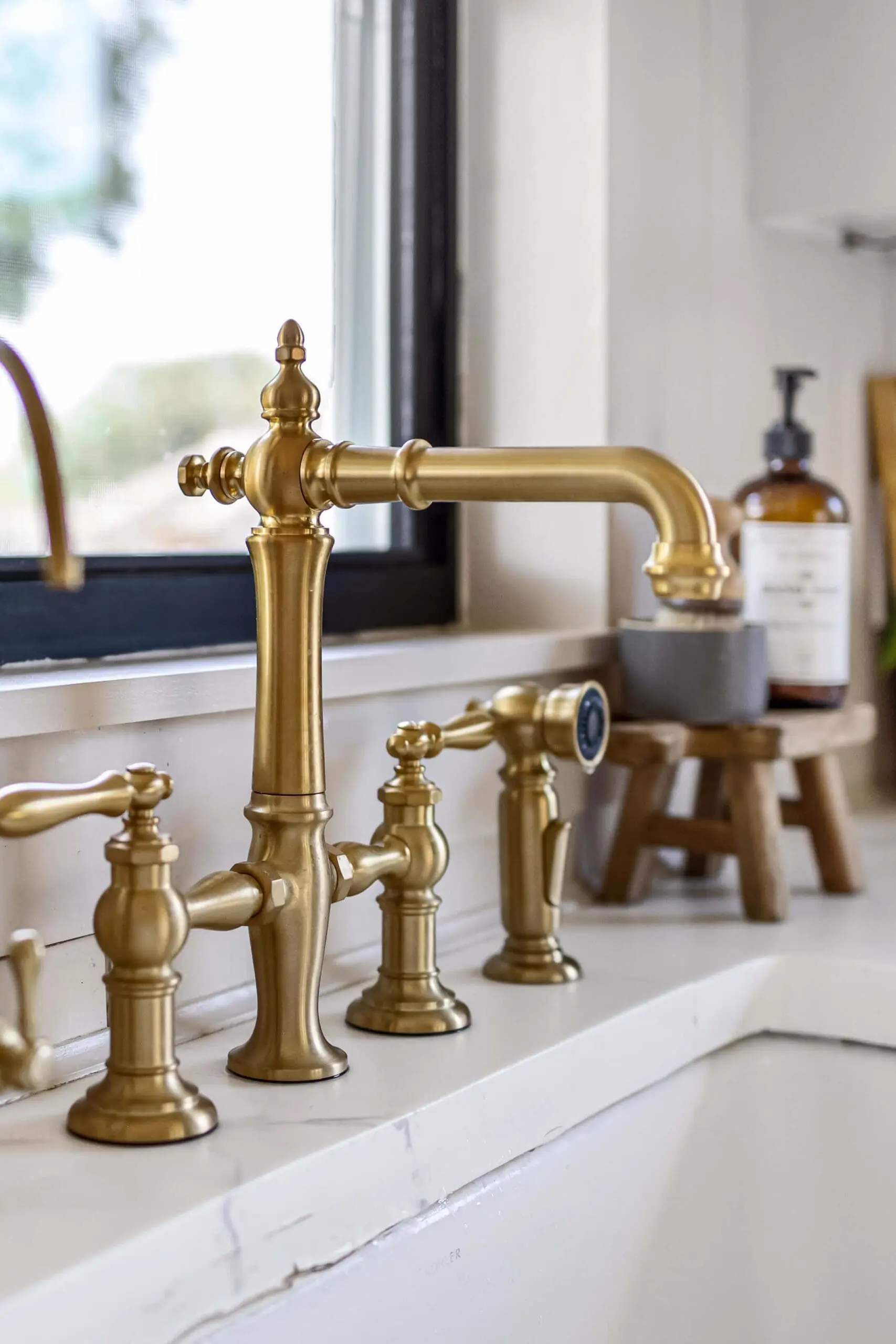 Detailed view of a gold bridge faucet mounted on white faux marble epoxy countertops with subtle gray veining