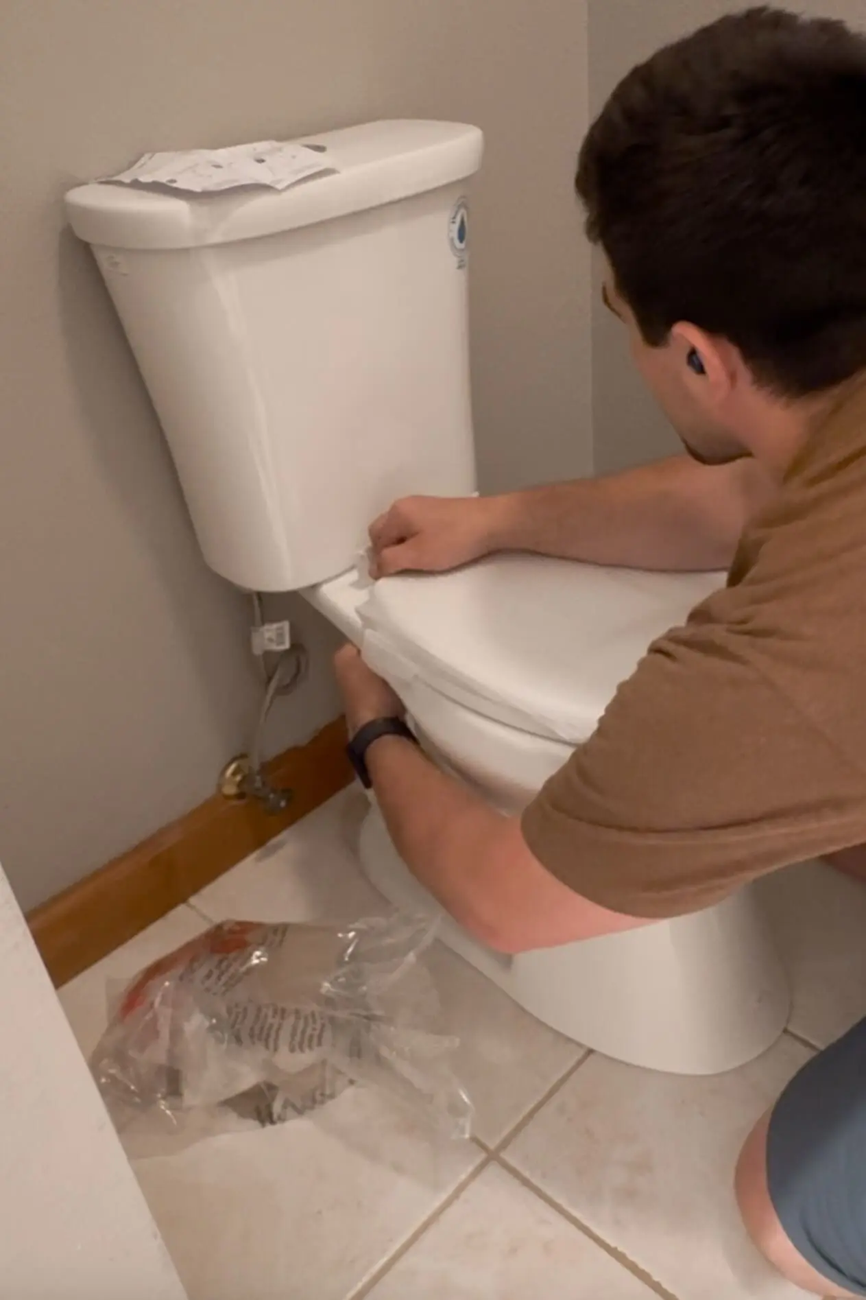 Man attaching the toilet seat to complete the final step of a DIY toilet installation in the primary bathroom.