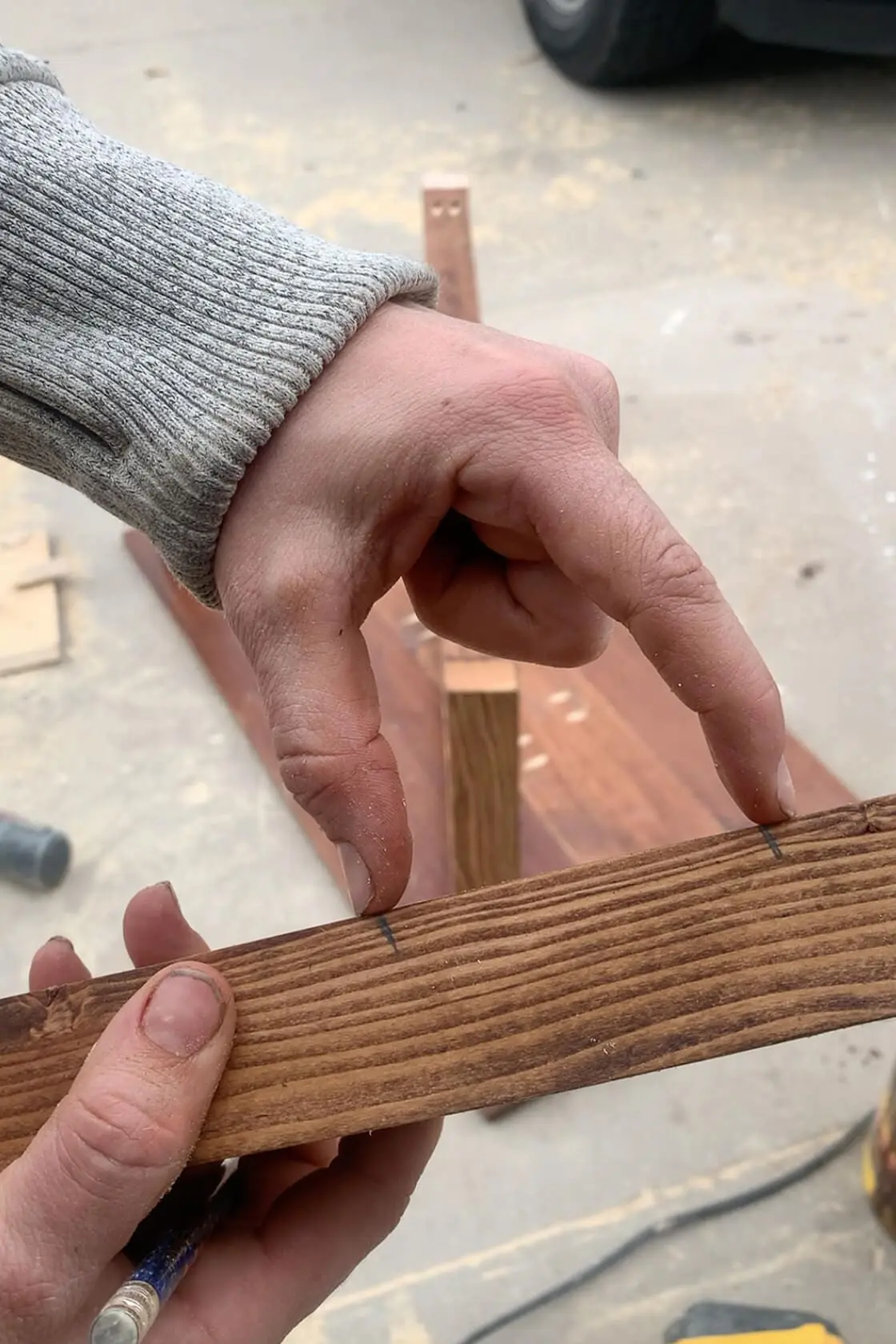 Close-up of hands marking measurement lines on a stained wood board during the DIY coffee table build process.