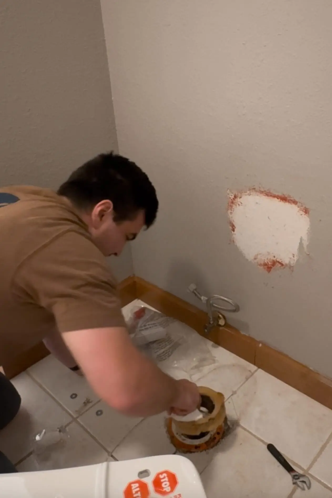 Man removing an old wax ring from the toilet flange during a DIY project to replace a toilet in the primary bathroom.