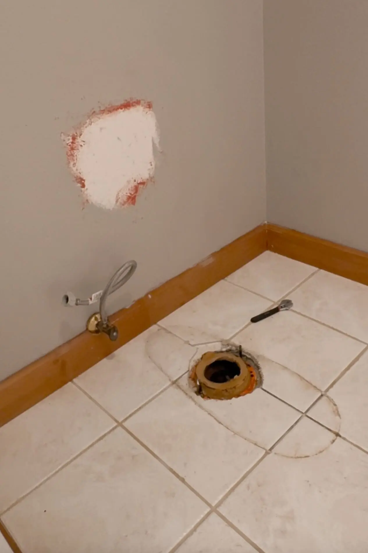 Bathroom floor with toilet removed, showing exposed toilet flange and old wax ring during the process of showing how to install a toilet.