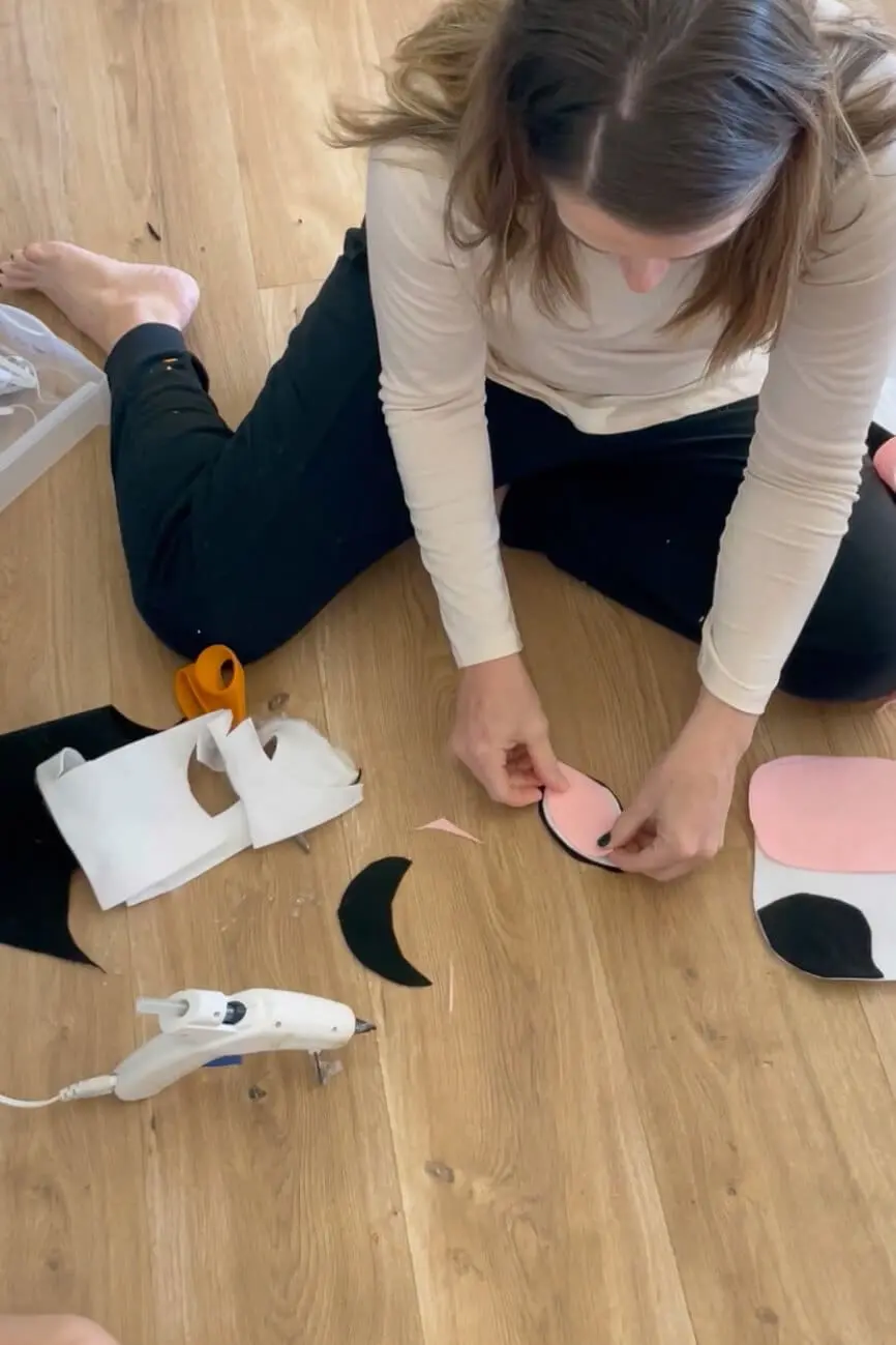 Attaching pink inner ear felt to black ear shapes while making a DIY cow costume mask.
