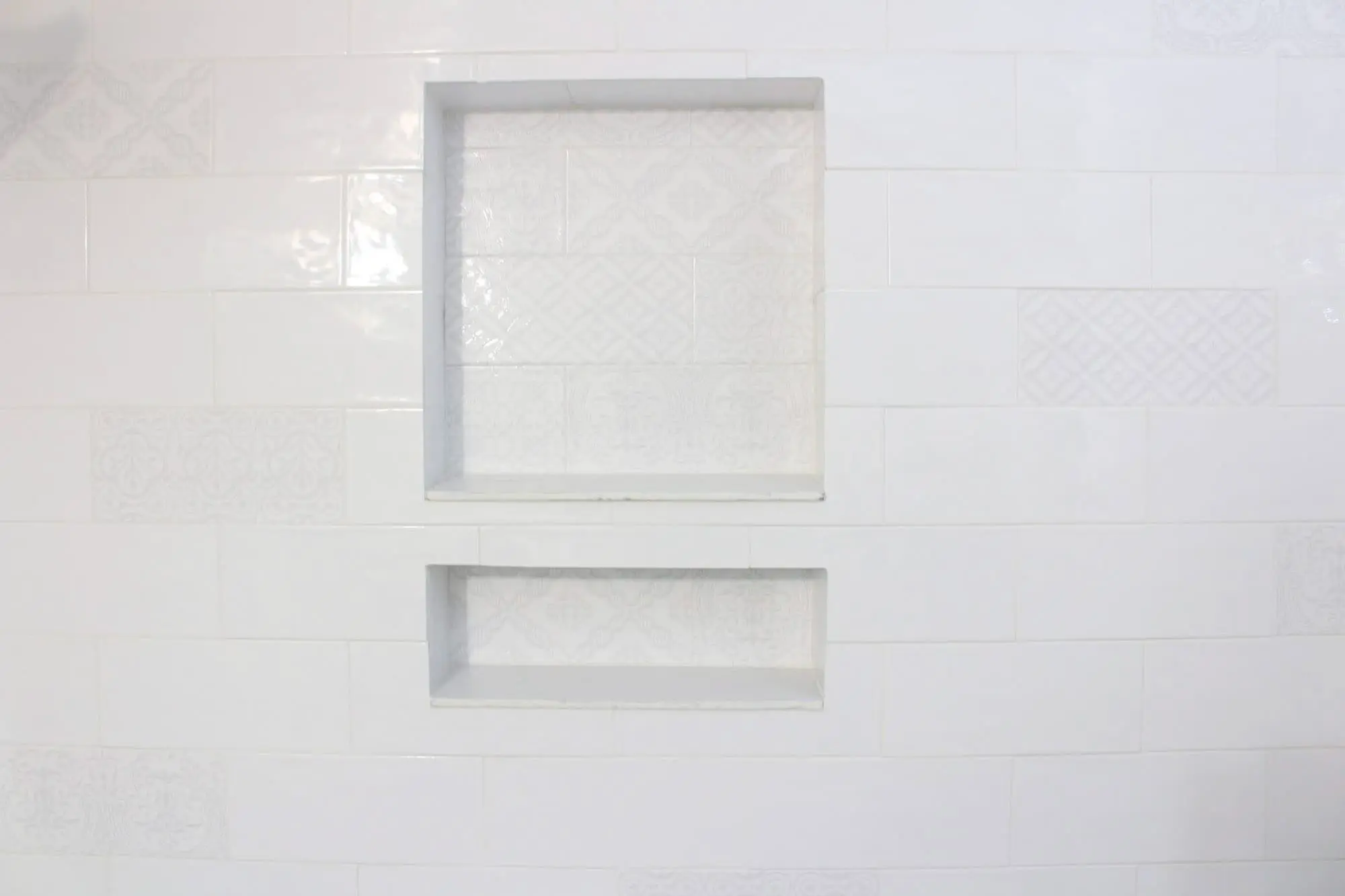 Built-in recessed double shower niches with white patterned tile backs set into a white subway tile shower wall.