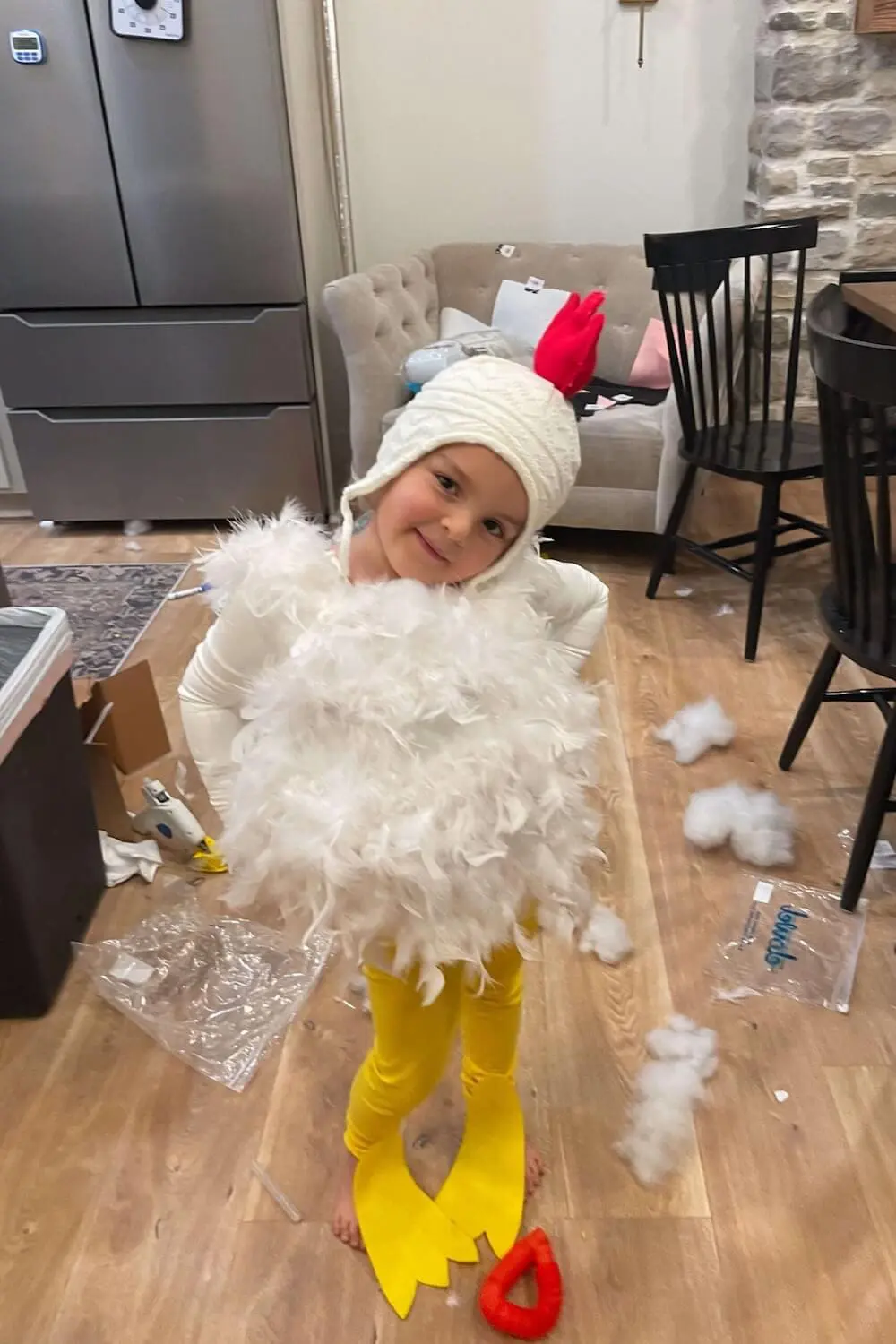 Child posing in a fluffy feathered chicken costume with yellow leggings and knit hat.