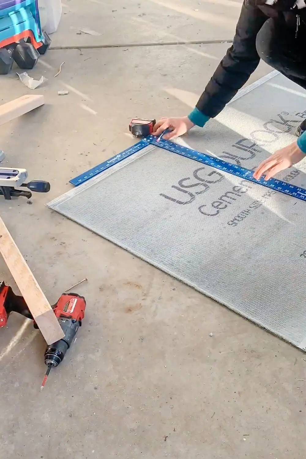 Measuring and cutting cement board with a carpenter’s square to fit around a shower niche opening.