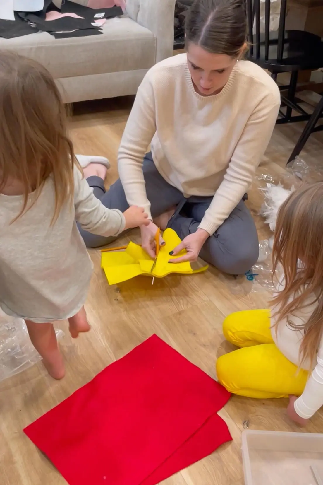 Mom cutting yellow felt into chicken feet shapes while two children watch and help during a costume-making project.