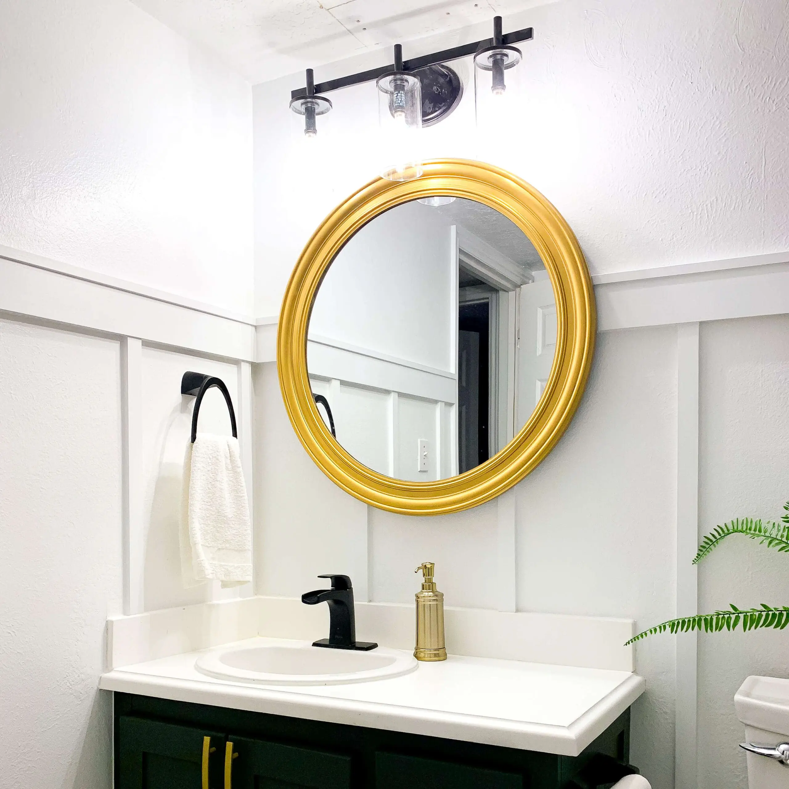 Round gold bathroom mirror makeover above vanity with black and white accents.