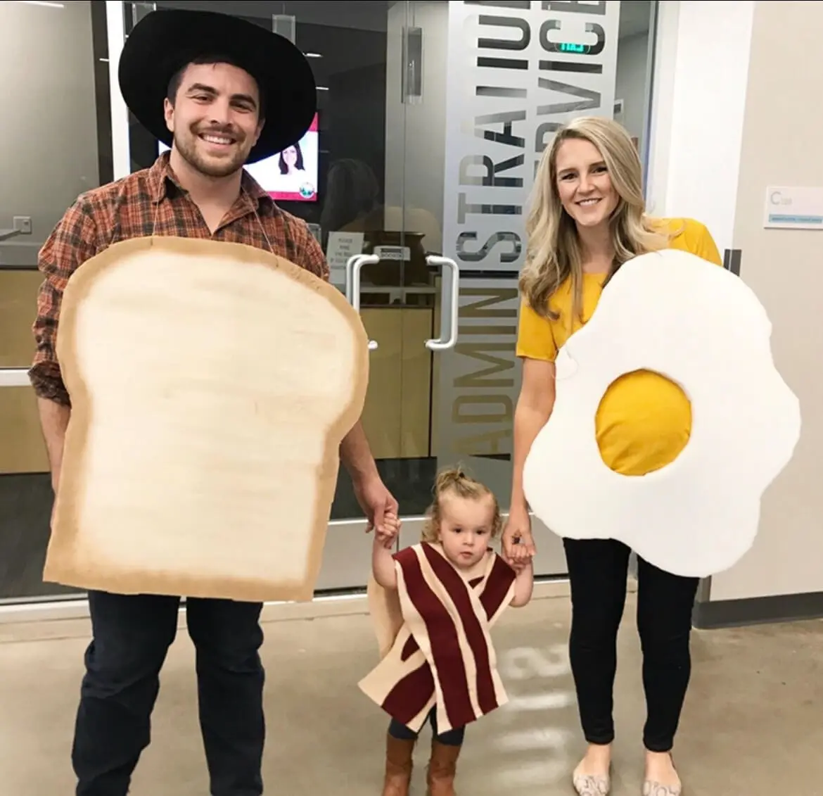 Family costume ideas for a breakfast theme, with parents dressed as toast and a fried egg, and a toddler as bacon.