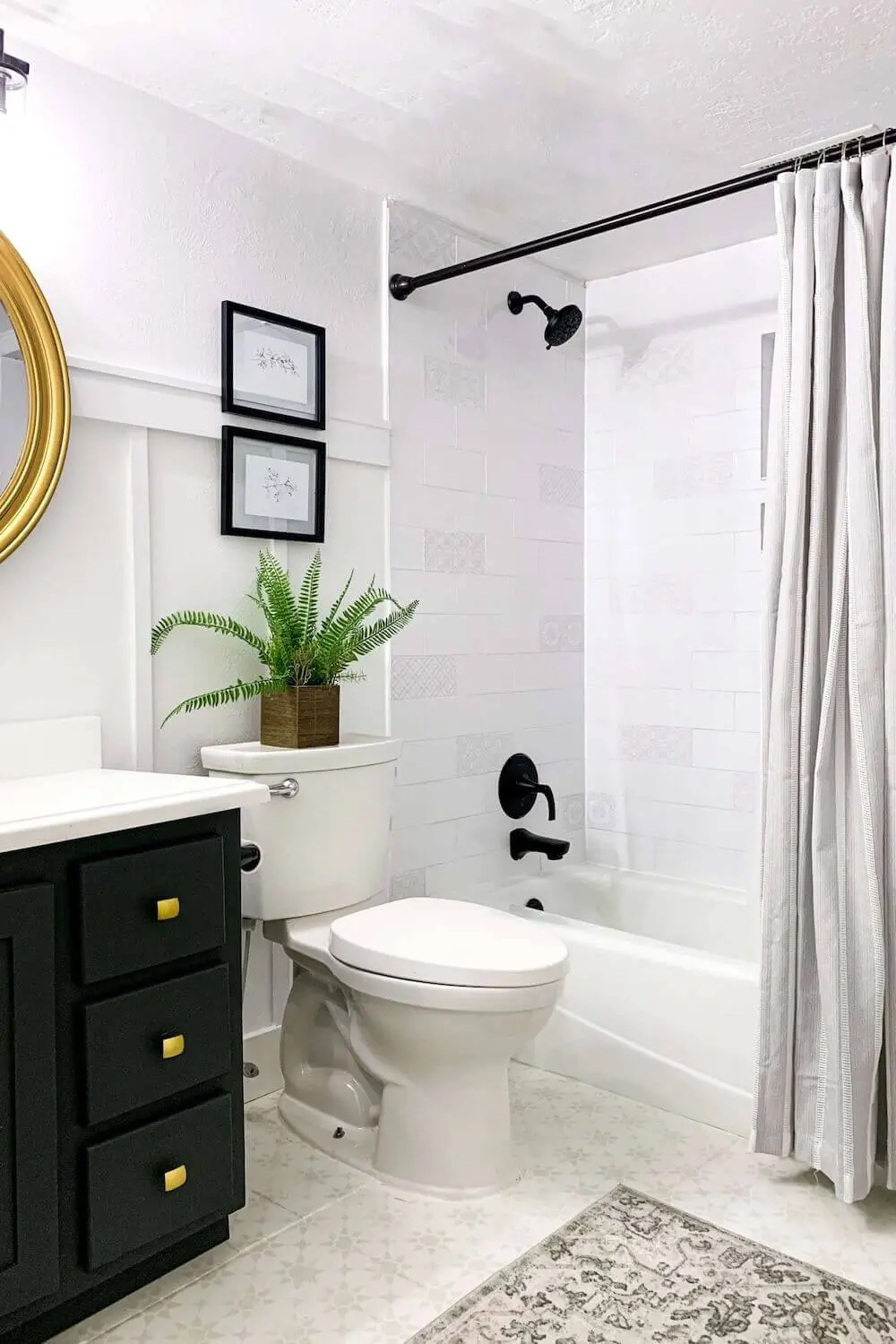 Wide view of remodeled small basement bathroom with green vanity, gold mirror, white subway tile shower, and patterned floor rug.