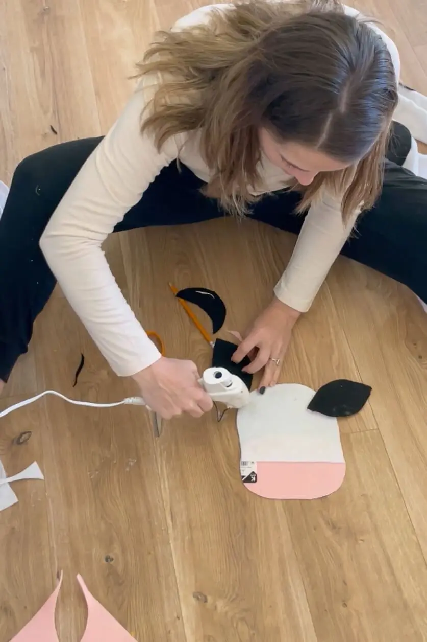 Gluing black felt cow ears onto a white and pink mask for a DIY cow costume.