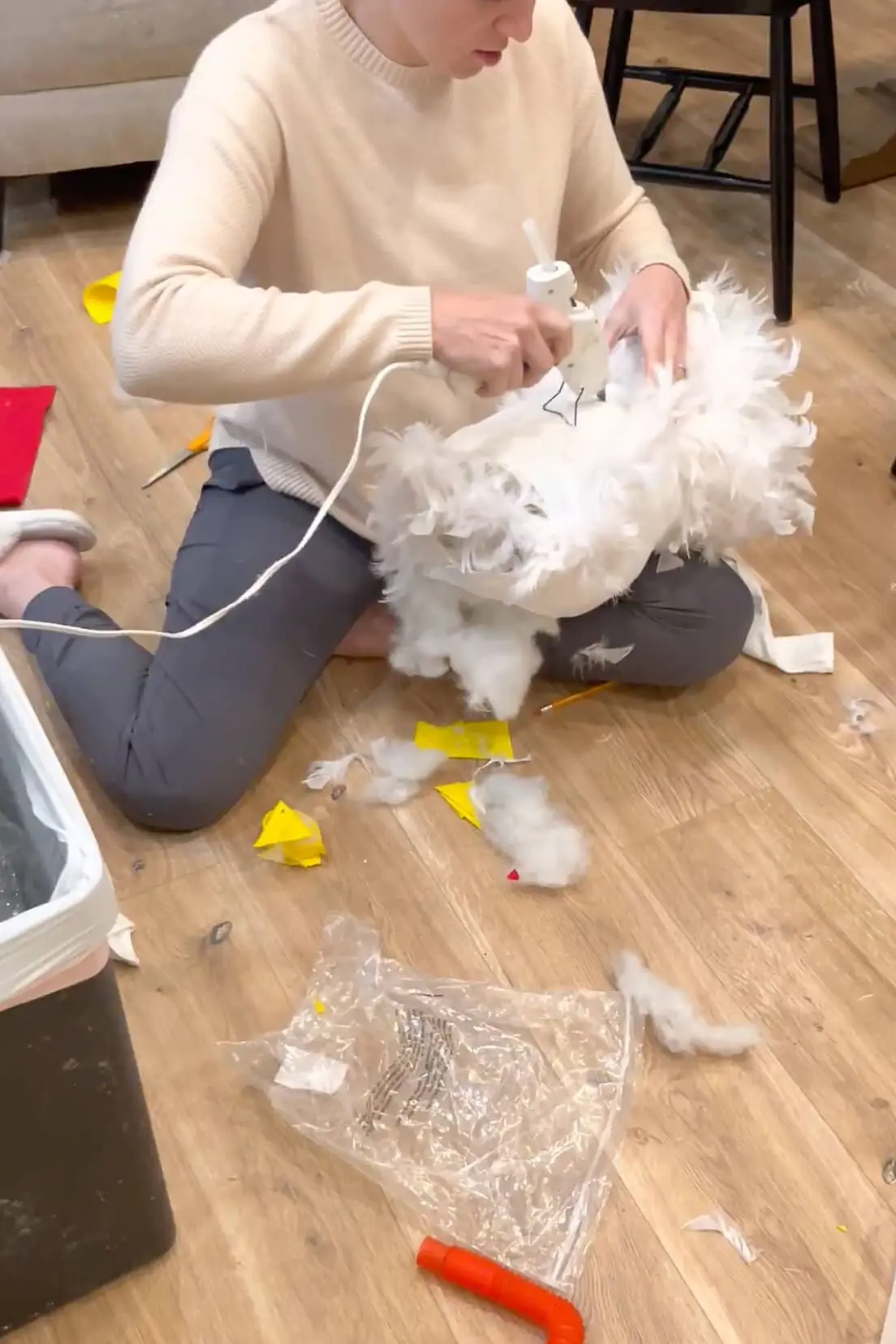 Mom using a hot glue gun to attach white feathers to the body of a handmade chicken costume.