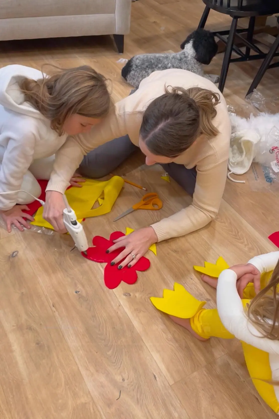 Mom and children using a hot glue gun to assemble red felt chicken combs and yellow felt feet for a homemade costume.