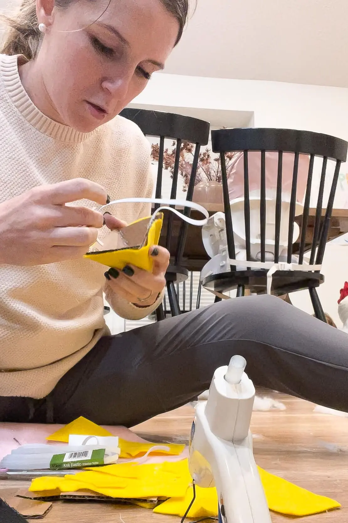 Mom applying hot glue to attach yellow felt to a cardboard triangle beak with an elastic band.