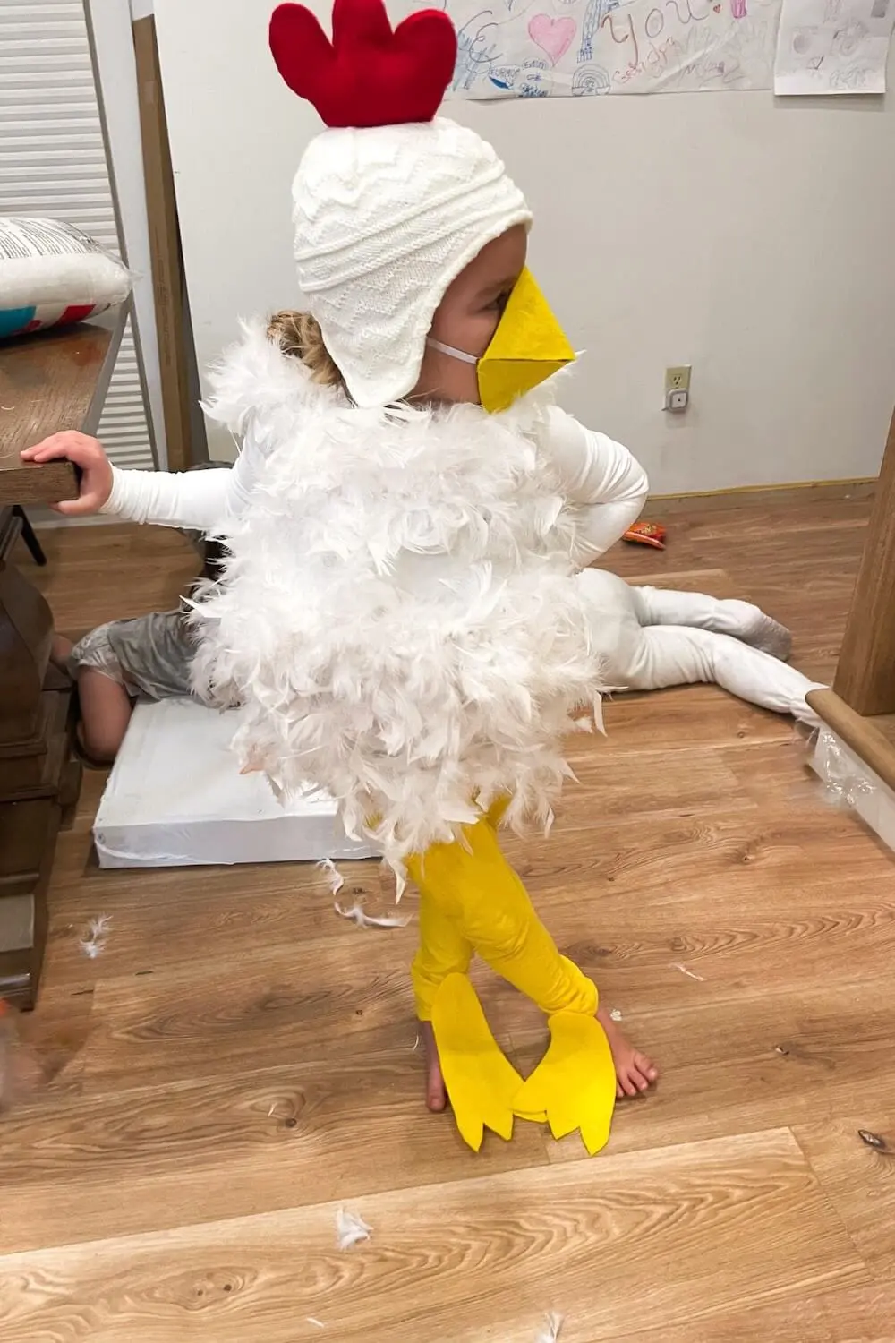 Child in a DIY chicken costume with white feathers, yellow leggings, and red felt comb.
