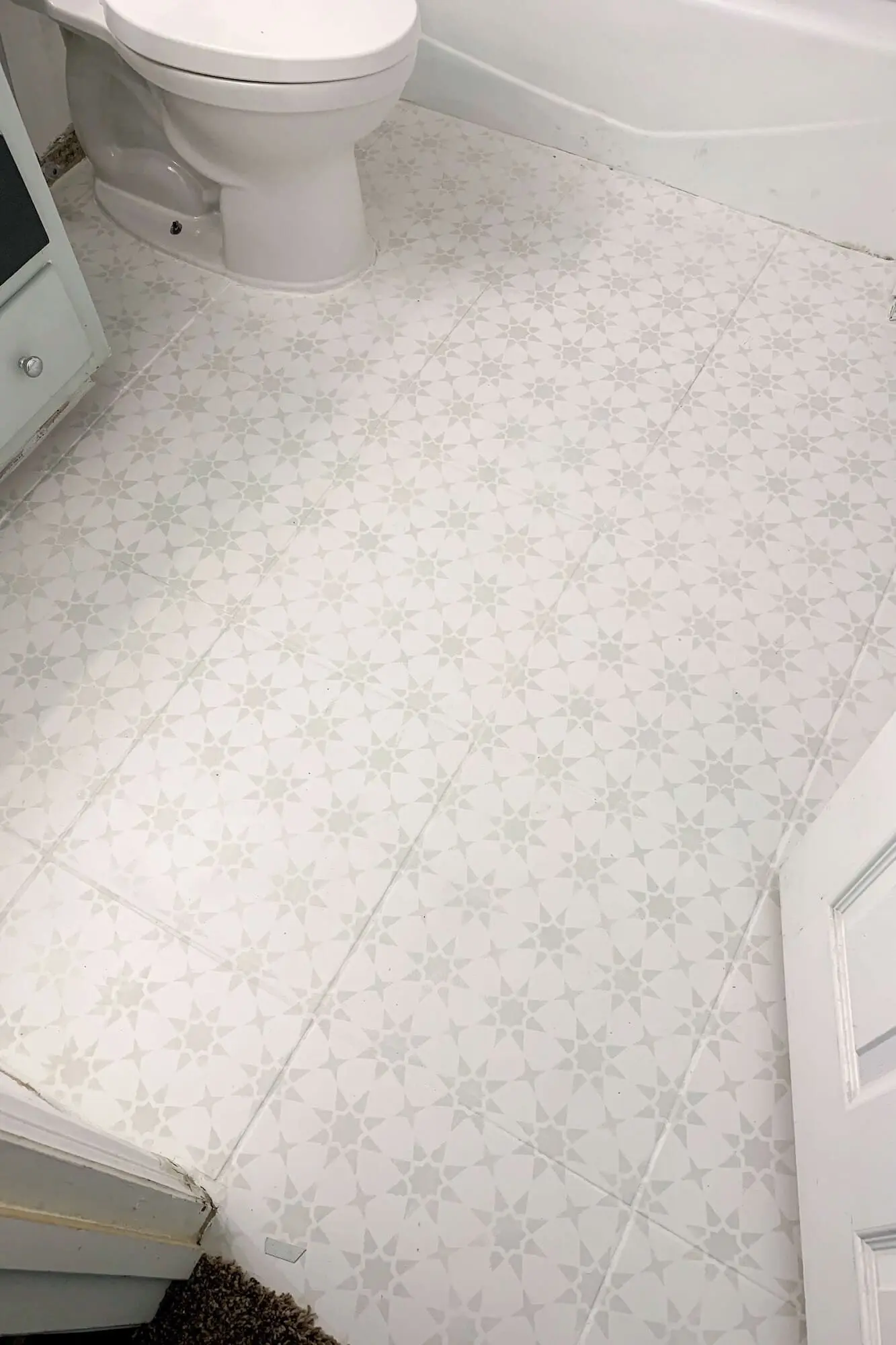 Overhead view of small bathroom floor makeover showing painted and stenciled tiles from doorway to tub.