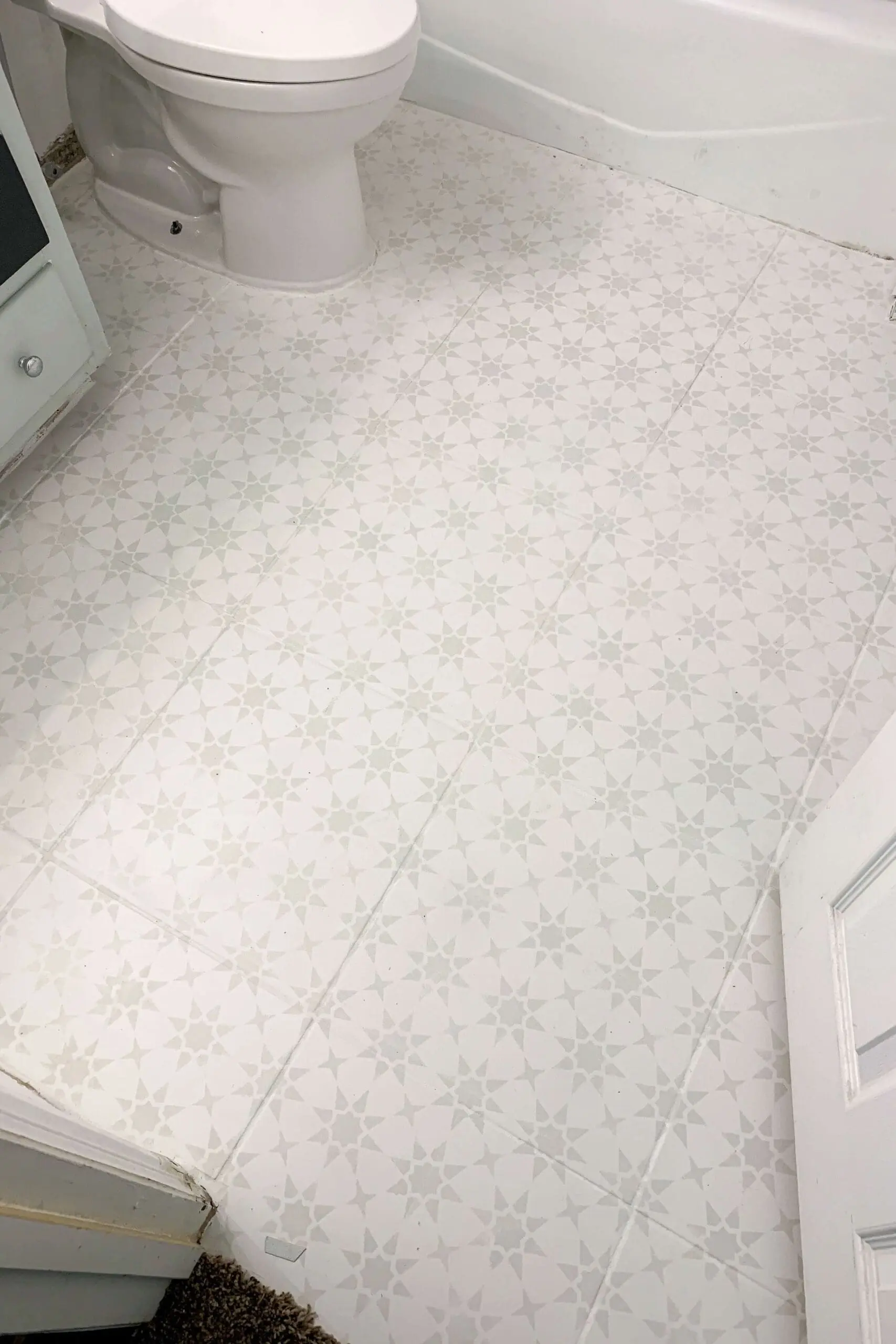 Full view of a small bathroom floor makeover showing freshly painted tiles with a repeating star stencil design, extending from the doorway around the toilet and bathtub.