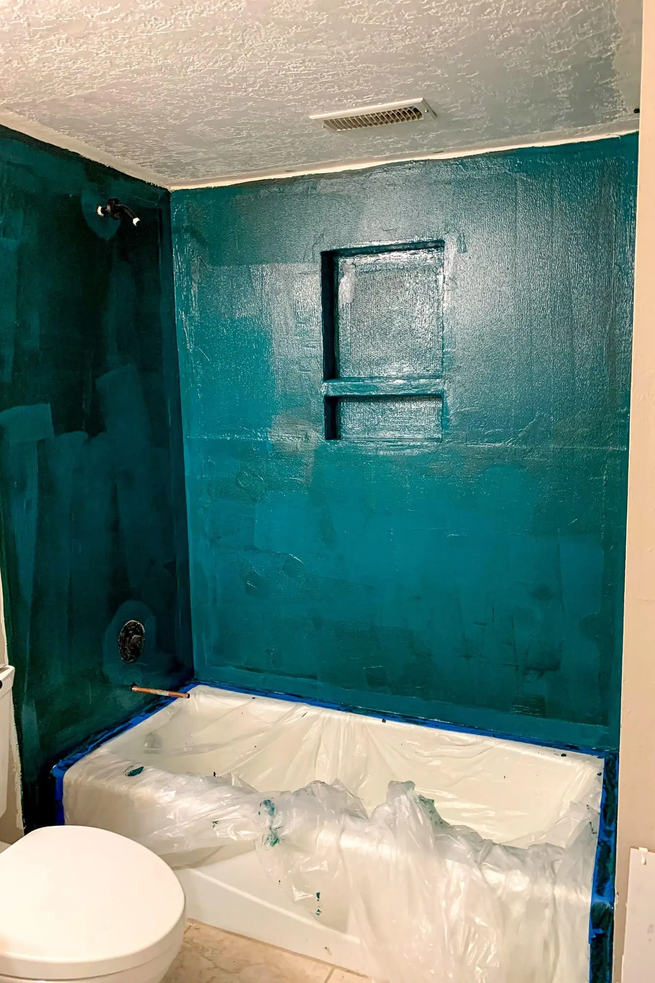 Applying the first coat of waterproofing membrane to shower walls during basement bathroom remodel, covering cement board completely.