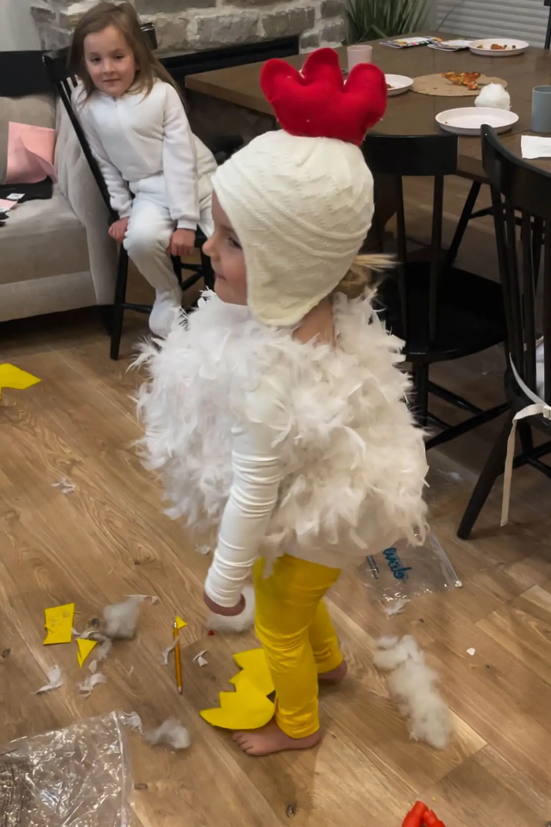 Side view of a child wearing a handmade chicken costume with white feathers, yellow leggings, and a knit hat with a red felt comb.