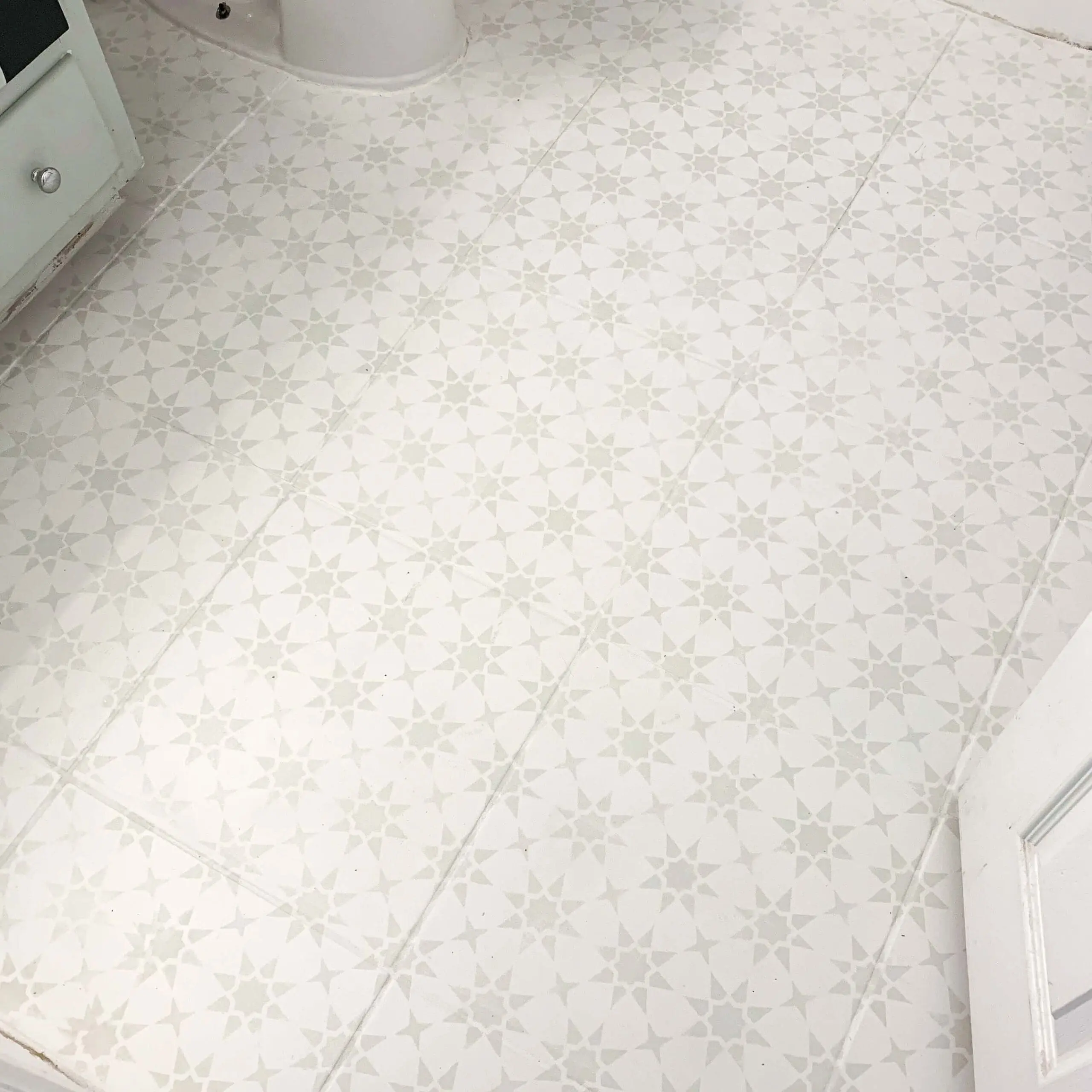 Detailed close-up of the stenciled star pattern painted over square bathroom tiles, showing the light gray design on a cream background near the base of the toilet and vanity.