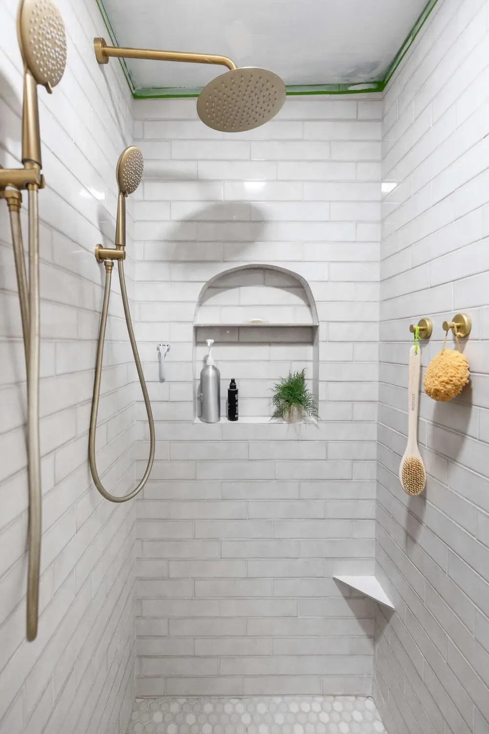 Walk-in shower with gold fixtures, arched shower niche, and light gray wall tile for a modern, elevated bathroom look.