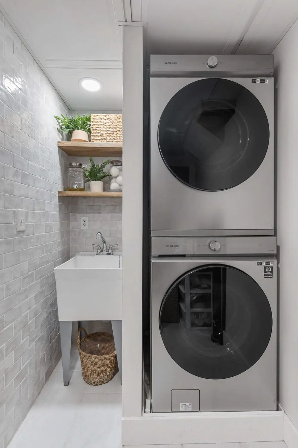 Basement laundry remodel with stacked washer and dryer, subway tile, and wood shelves.