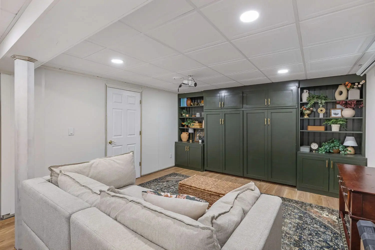 Cozy basement living room after DIY home remodel with green built-ins, projector, and sectional sofa.