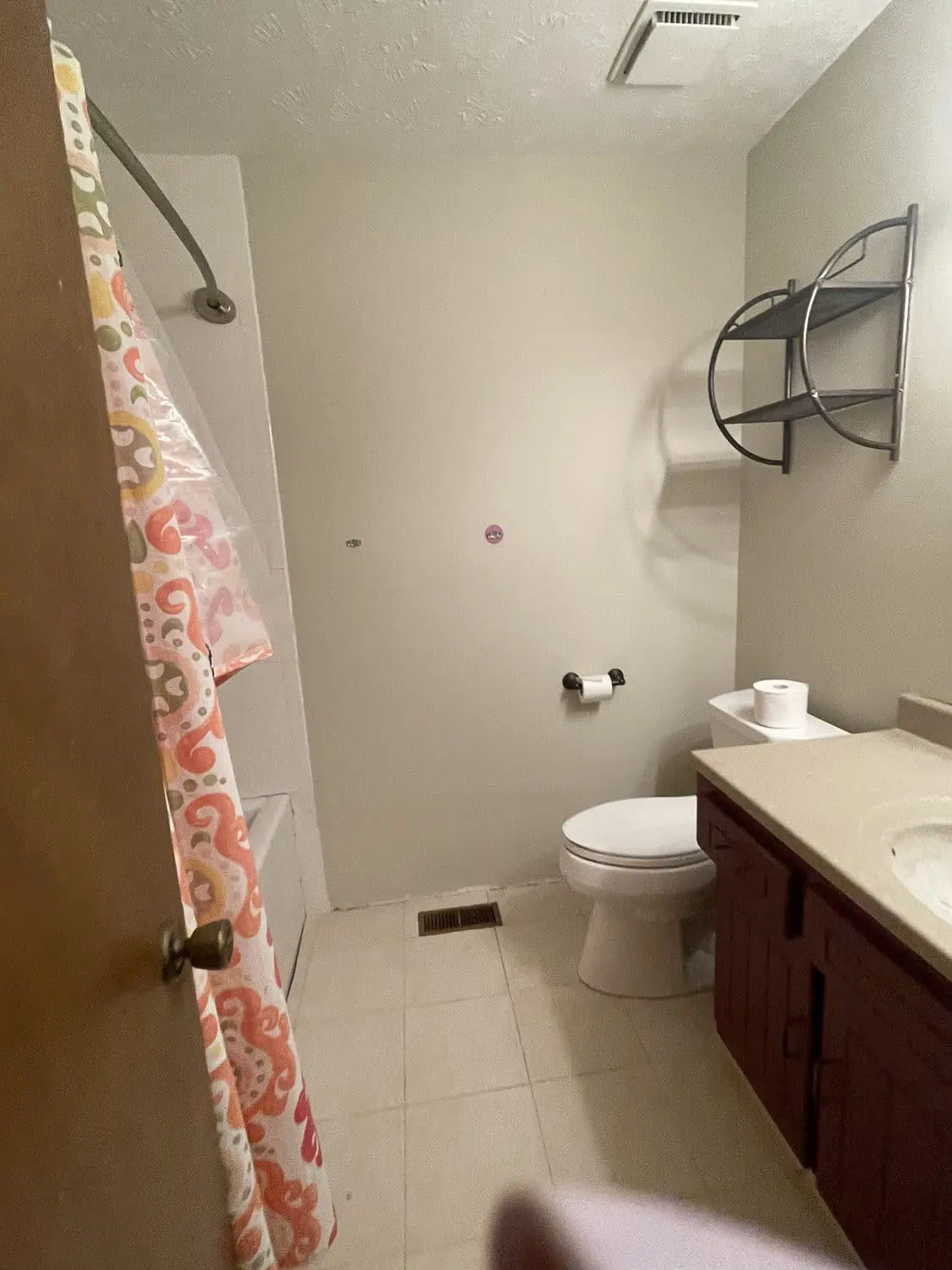 Outdated bathroom before remodel with beige tile, dated vanity, and shower curtain.