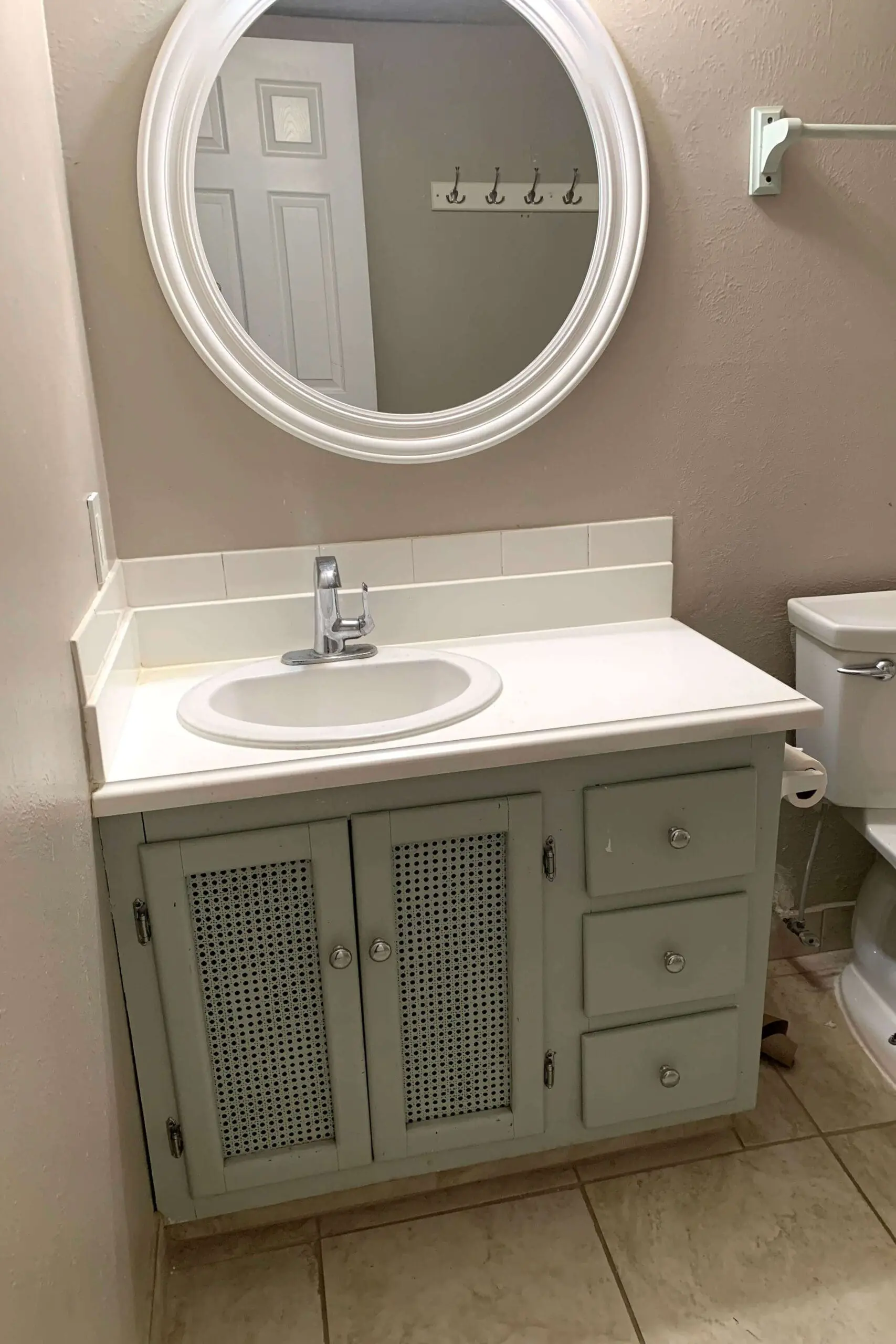 Close-up of worn green bathroom cabinet with scuffed finish and dated knobs before painting.