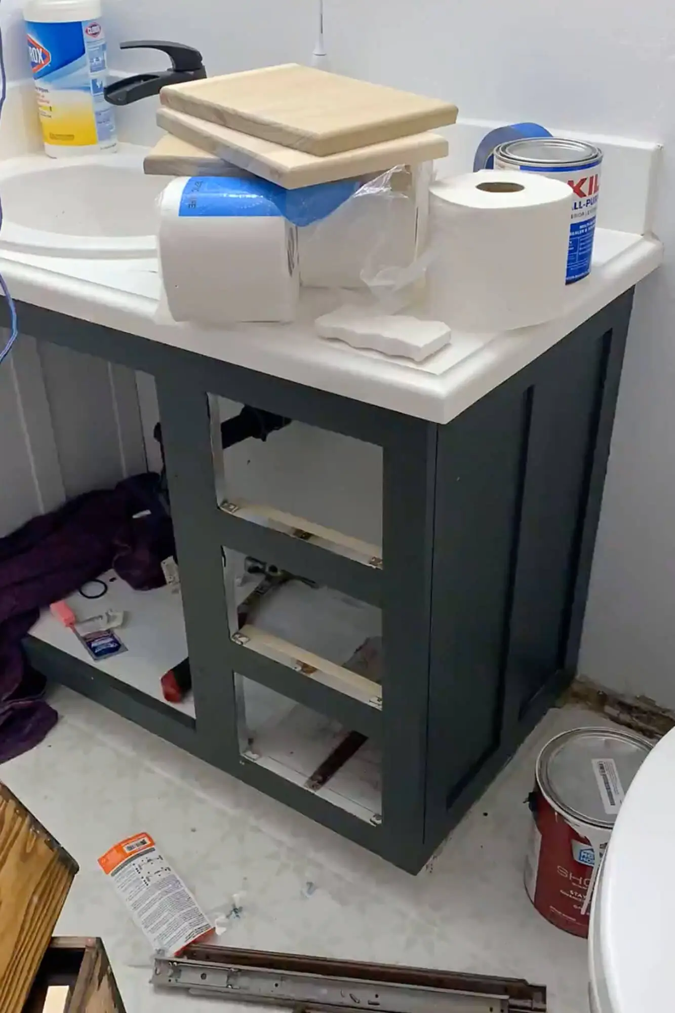 Bathroom vanity frame with new drawer fronts removed and supplies stacked on the countertop