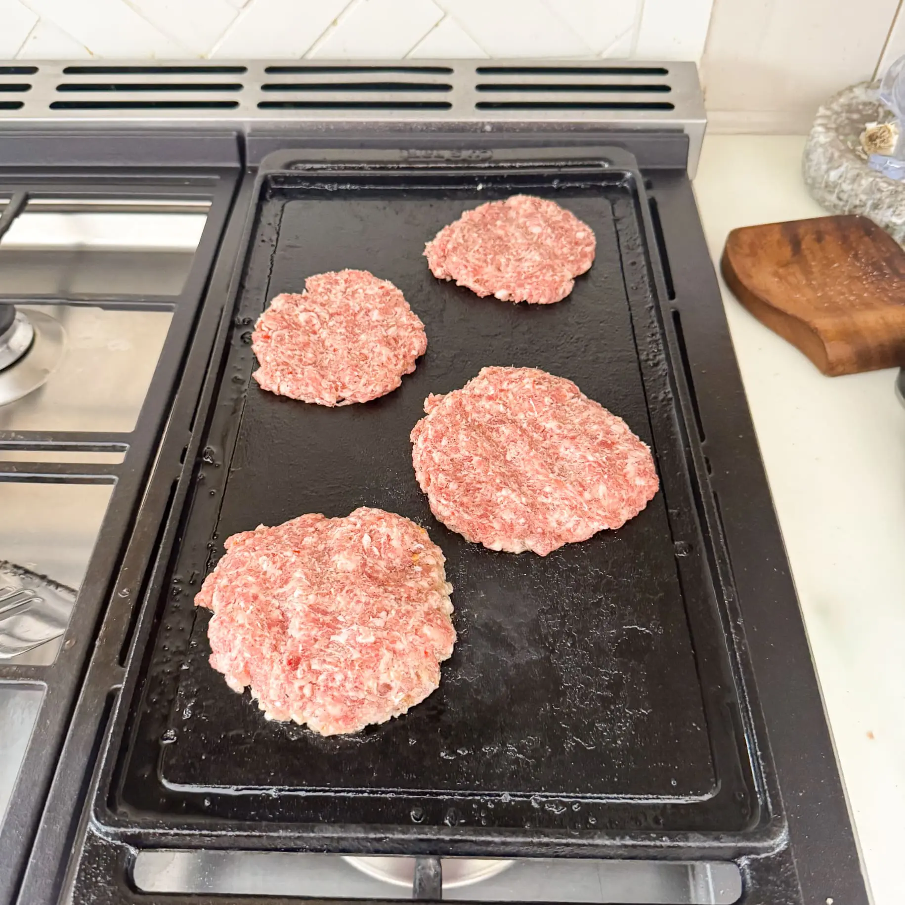 Raw sausage patties cooking on a stovetop griddle for a homemade carnivore breakfast.