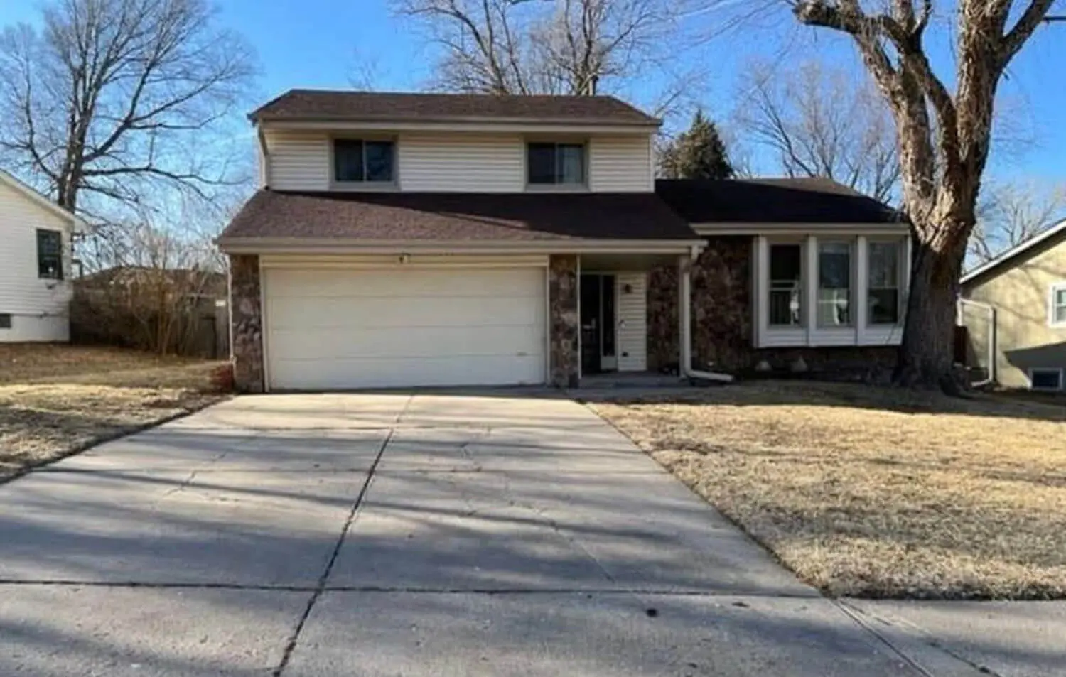 Exterior of split-level house before remodel with dated siding and plain garage door.