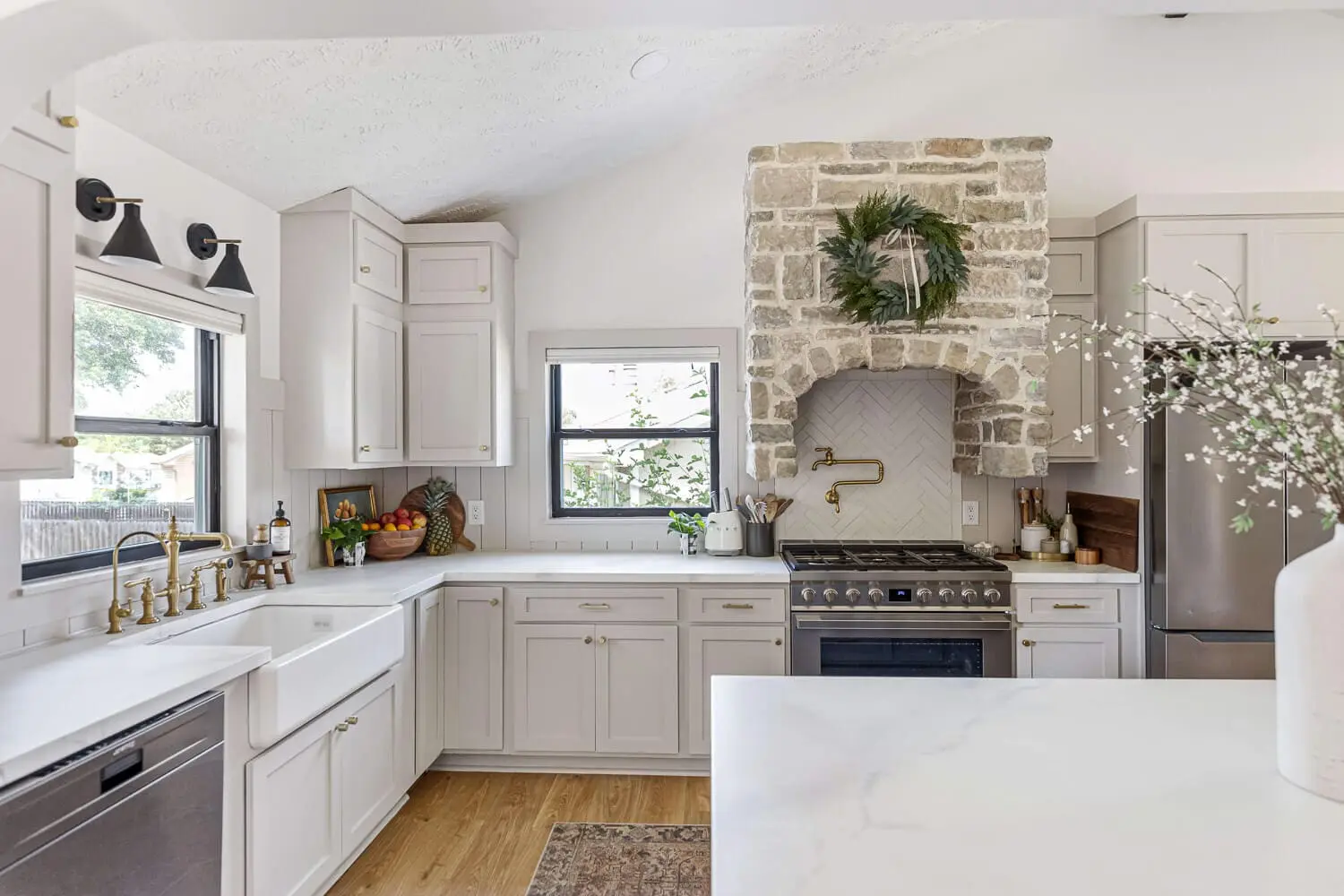 Remodeled kitchen with stone range hood, brass pot filler, and farmhouse sink