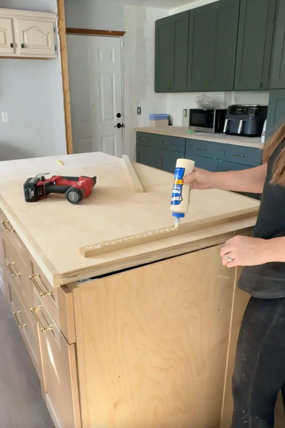 Close-up of DIY counter build, applying wood glue to edge trim on a plywood island before transforming it with contact paper.