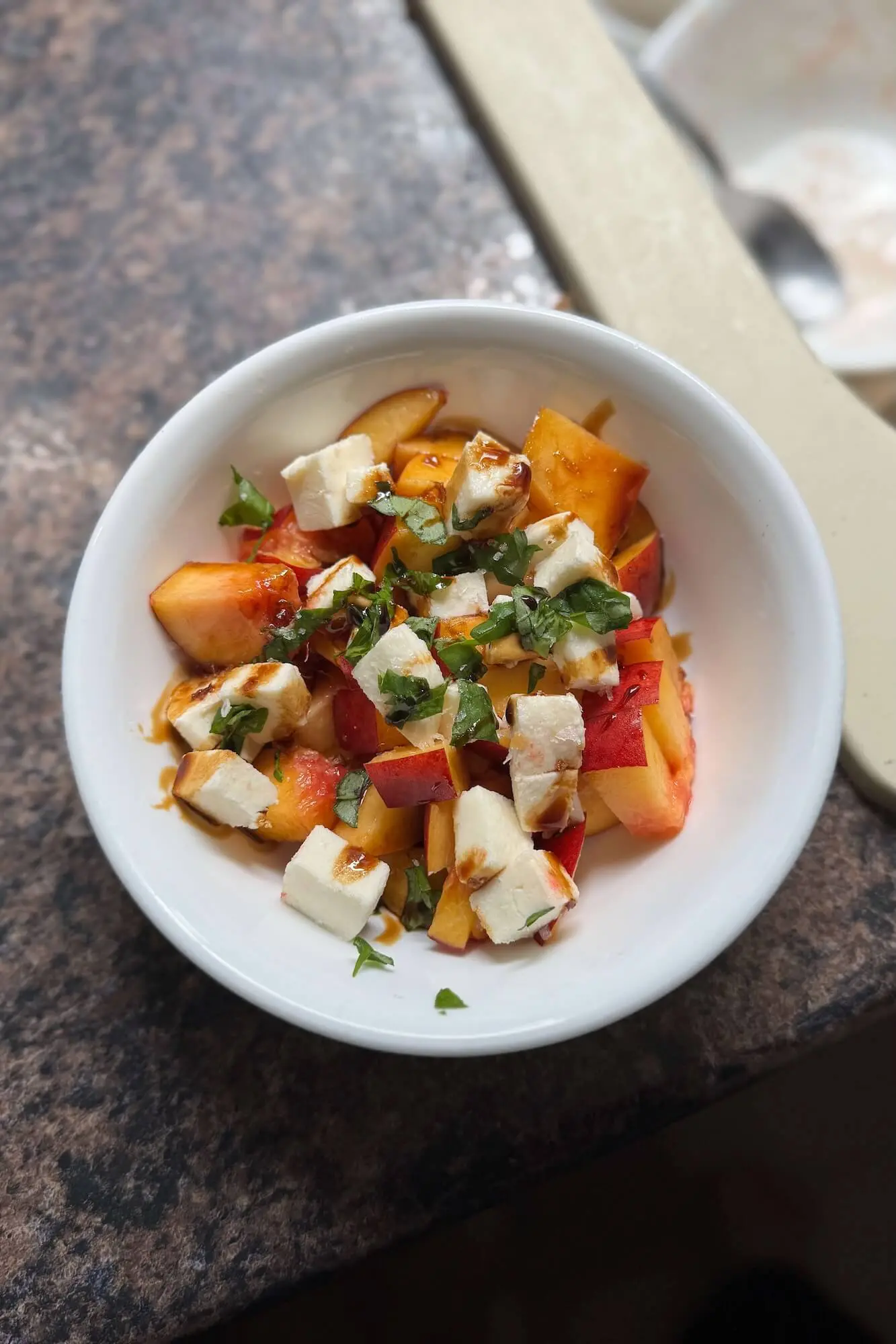 Nectarine salad with mozzarella and basil topped with balsamic glaze in a round white bowl, photographed from above.