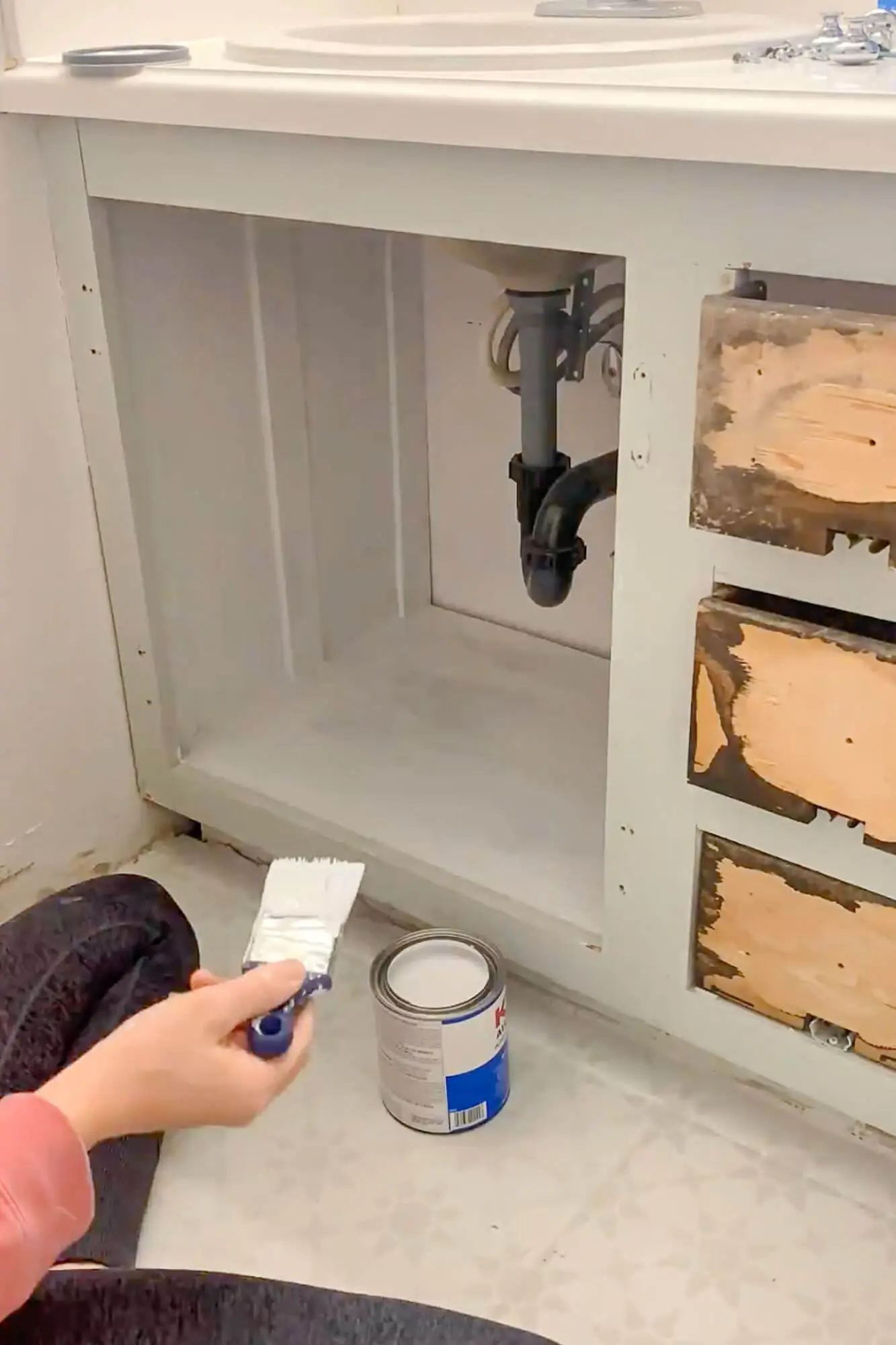 Priming the inside of a bathroom vanity cabinet with a paint brush