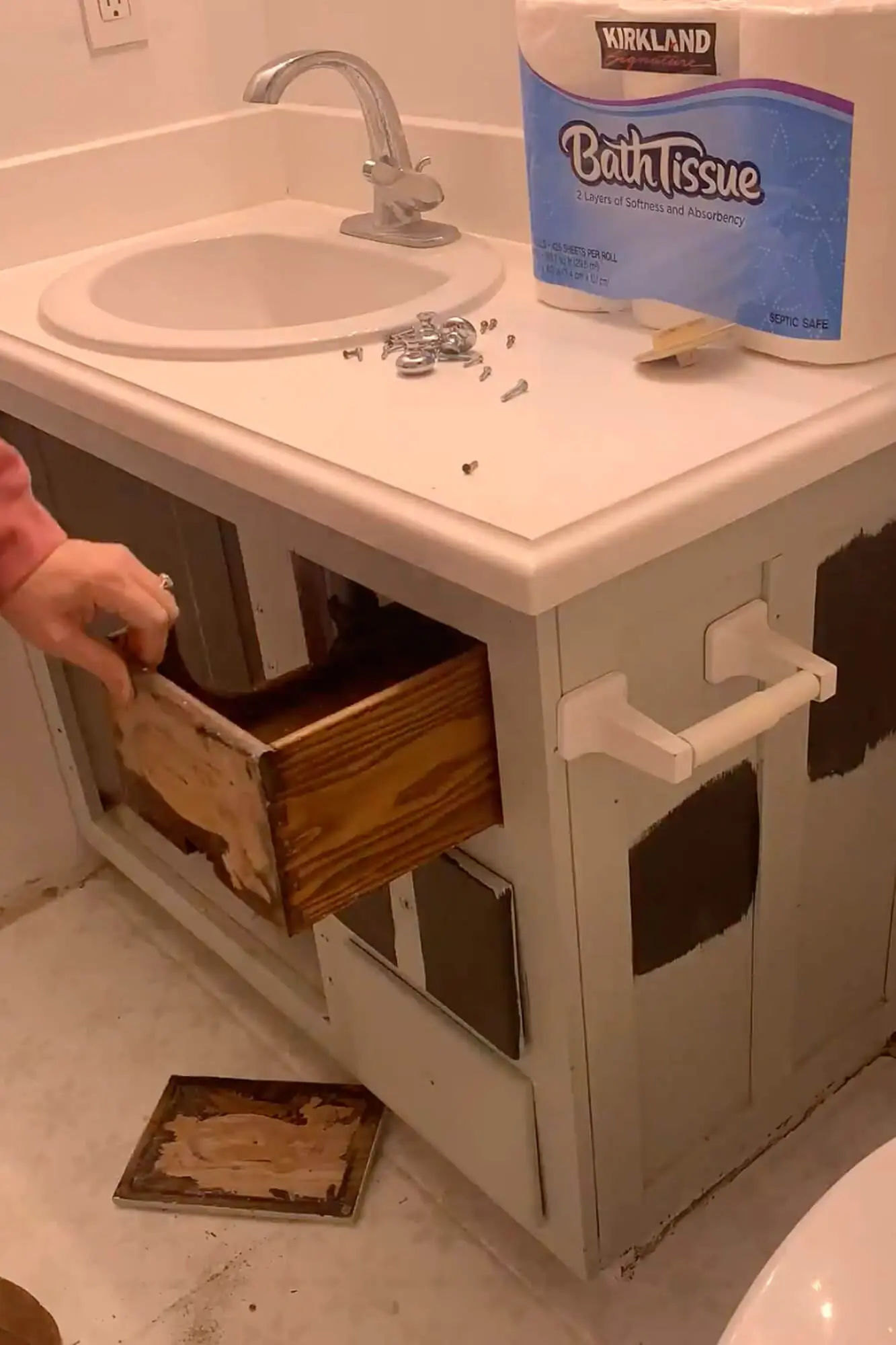 Removing an old drawer front from the bathroom vanity during DIY cabinet prep, with hardware and supplies on the countertop.