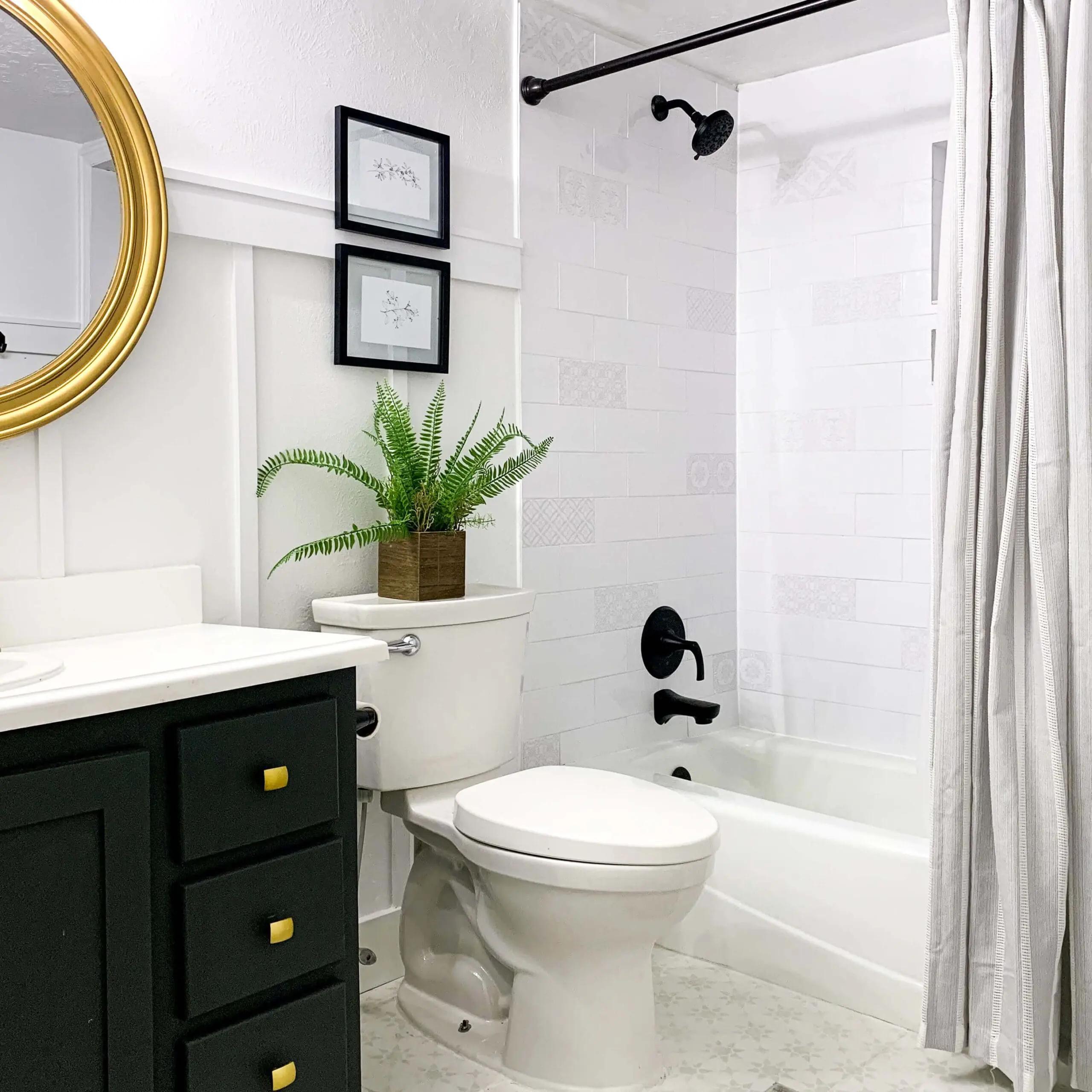 Stylish small bathroom makeover featuring green vanity, board and batten walls, black hardware, and tiled bathtub.