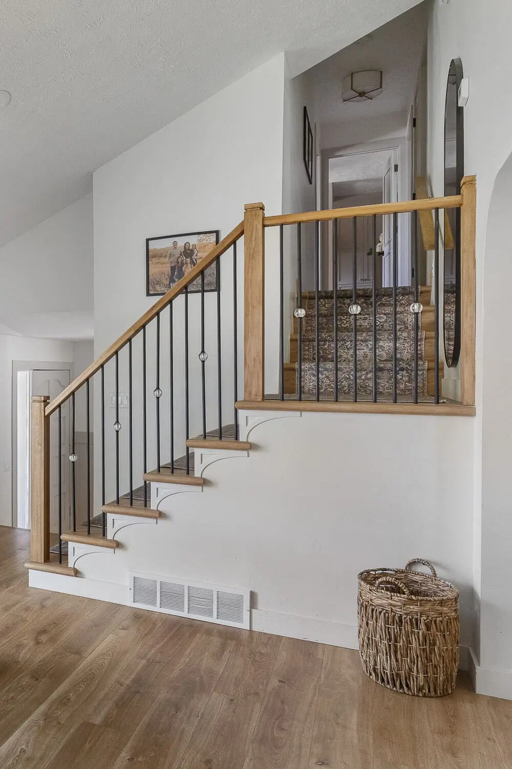 Home remodel before and after of staircase with black iron spindles and light neutral walls.