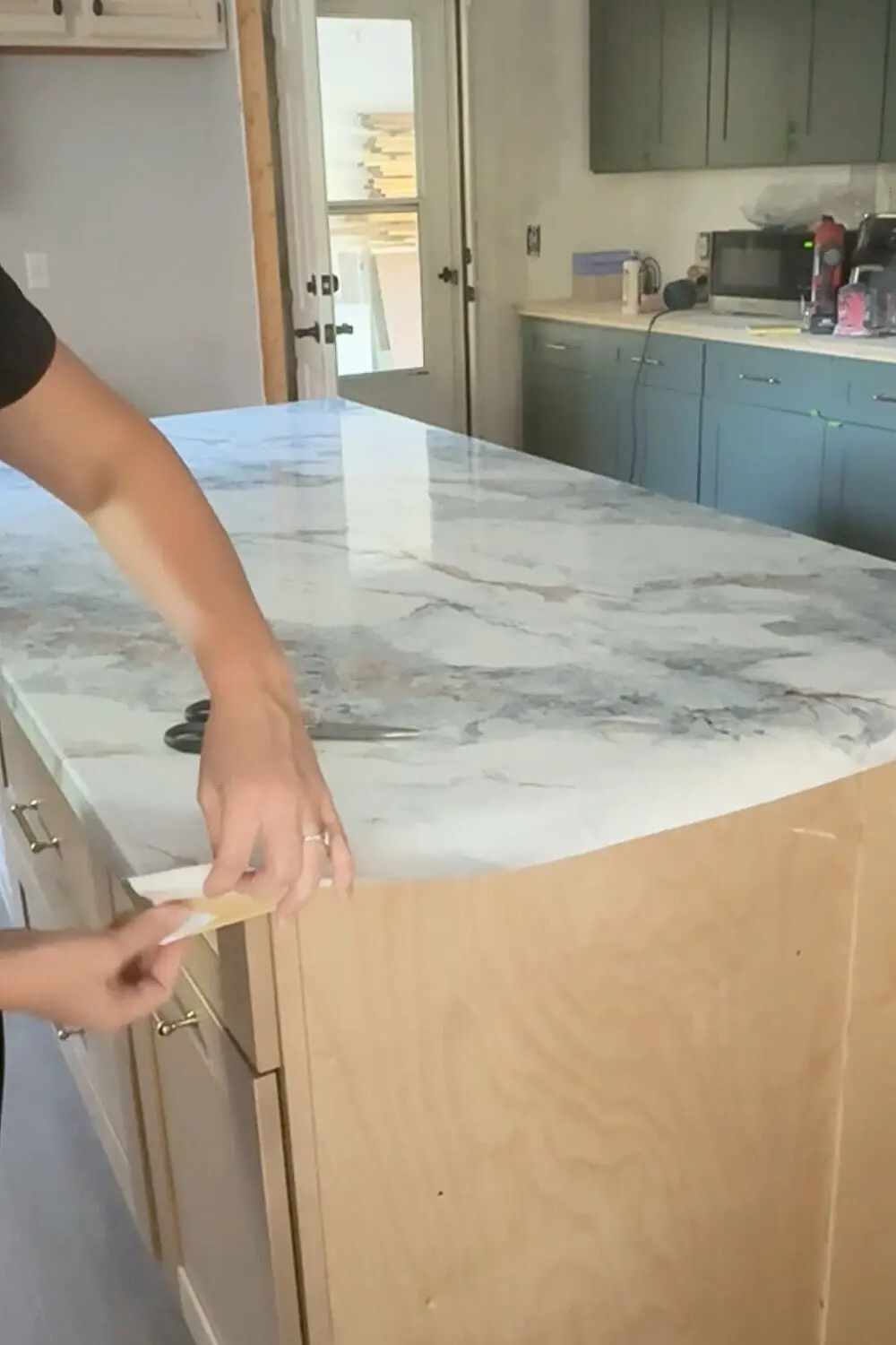 Wrapping marble contact paper around the edge of a kitchen island countertop, trimming for a clean finish in a DIY faux marble makeover.
