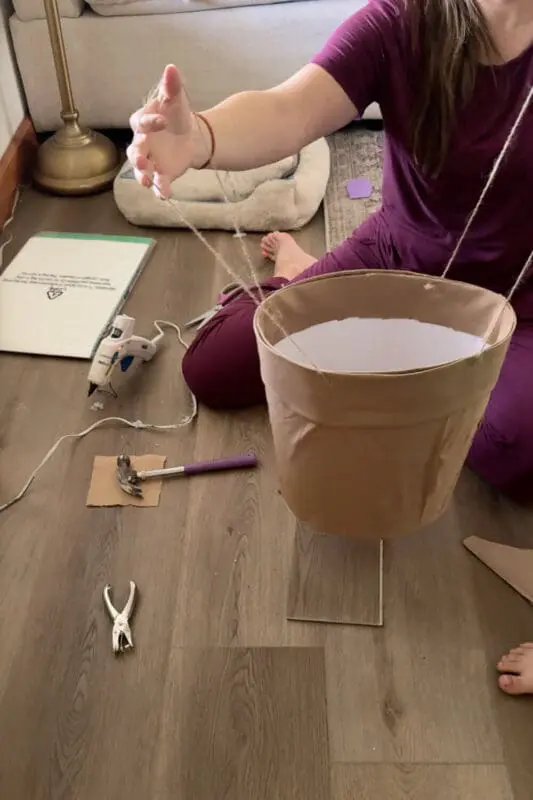 Attaching twine straps to the finished flower-pot skirt so kids can wear the no sew cardstock flower costume hands free.
