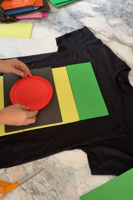 Hands placing a red lid on top of black, yellow, and green foam sheets while assembling a DIY craft design for a funny Halloween look.