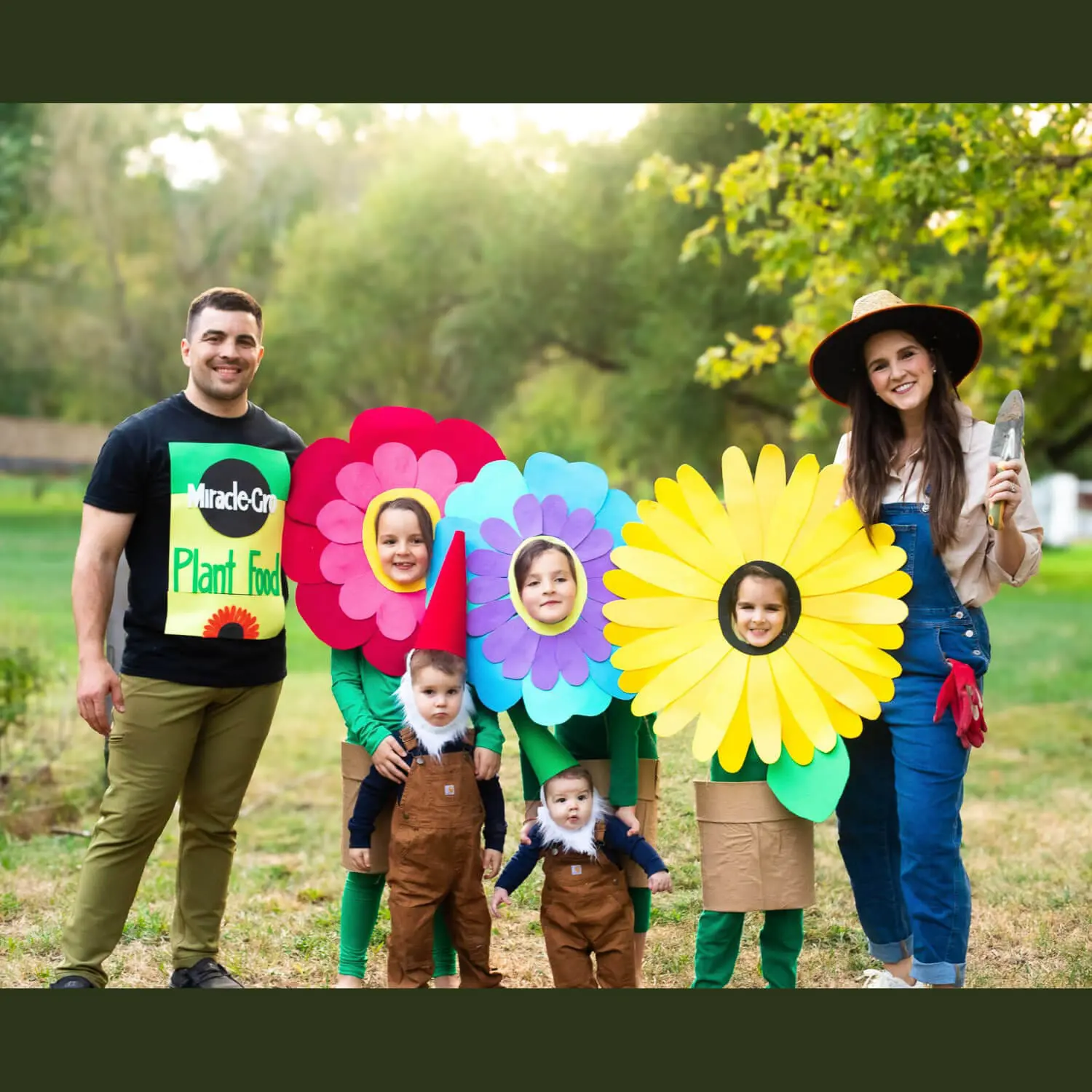 DIY family costume, garden theme: dad in Miracle-Gro plant food shirt, three kids as giant paper flowers, two toddlers as garden gnomes, and mom dressed as a gardener with a trowel.