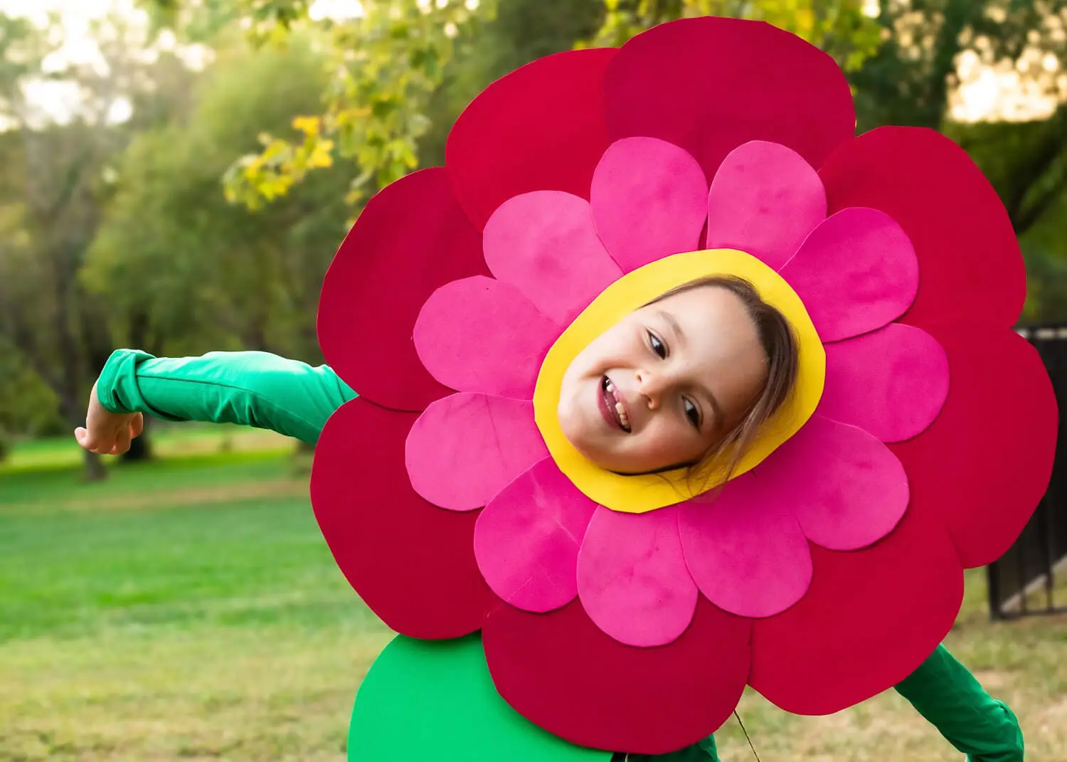 Child in a DIY flower costume with layered red and pink petal headpiece and green stem outfit