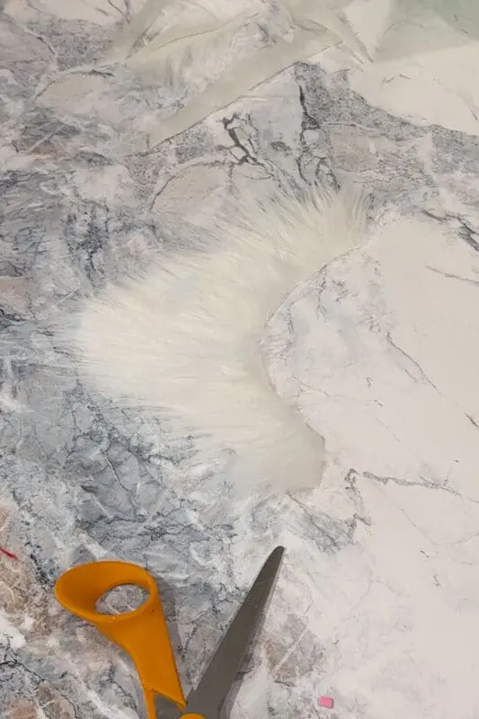 Cutting white faux fur into a curved beard shape on a marble counter for a DIY kids Halloween outfit.